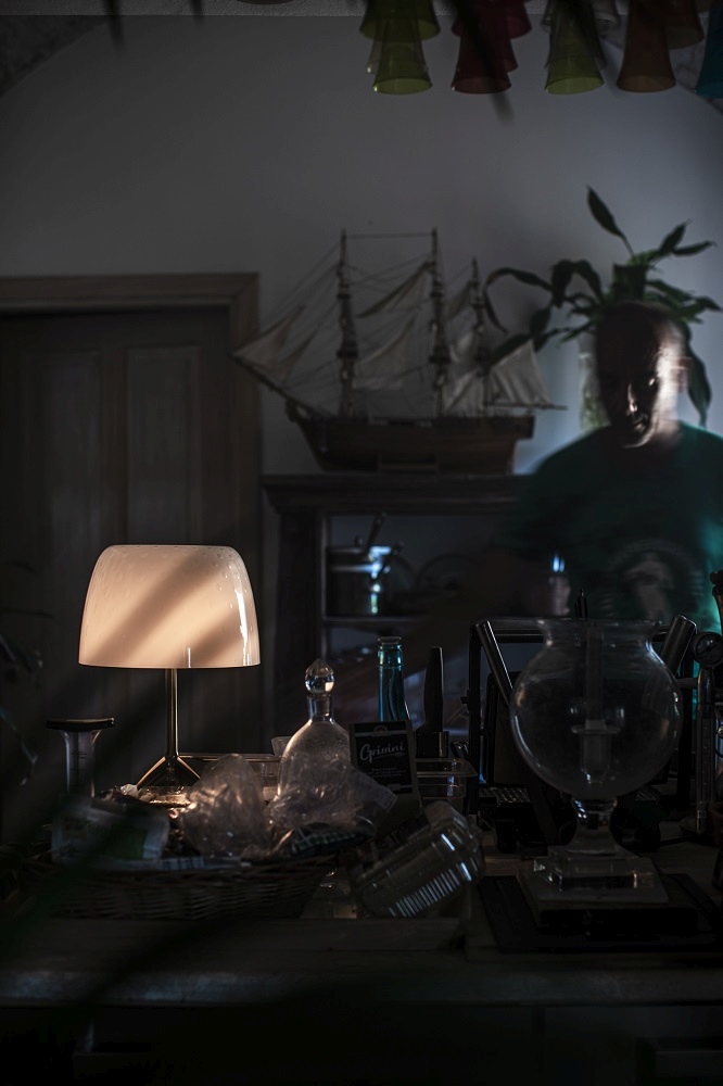 Nahaufnahme der Lumiere Tischleuchte von Foscarini, die ein warmes Licht auf einem überladenen Tisch wirft.