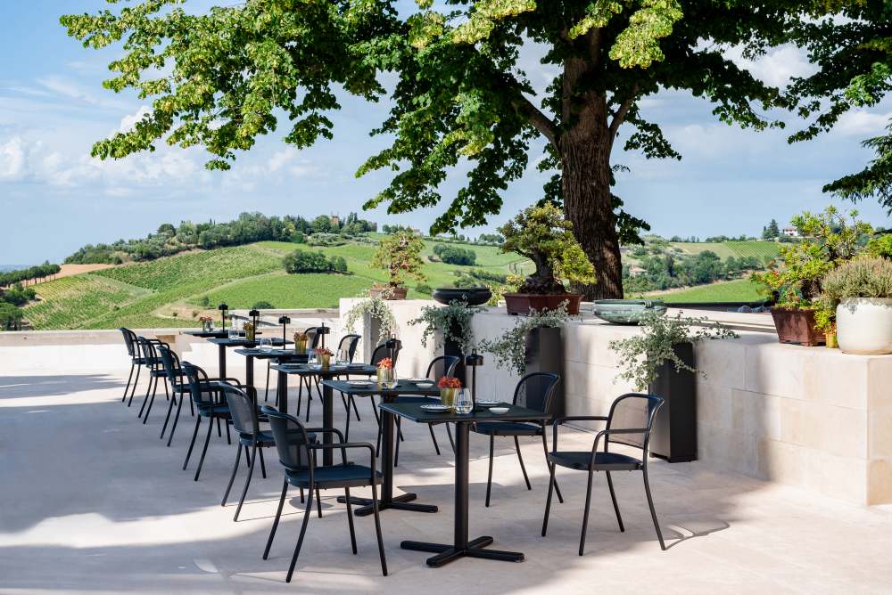 Café Chair Stuhl Outdoor Emu: Schwarze Metallstühle und Tische auf einer Terrasse mit Landschaft.
