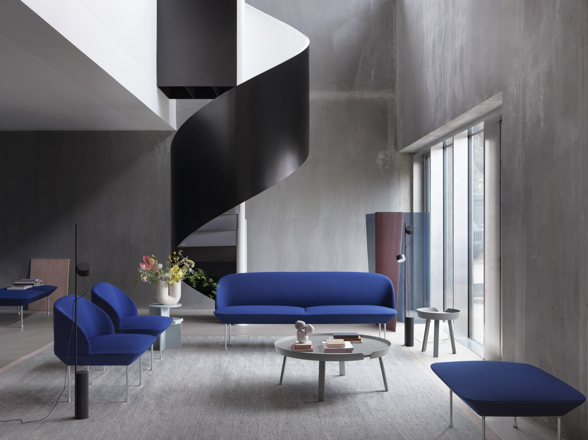 Blaues Oslo Sofa von Muuto in modernem Wohnzimmer mit Designermöbeln und Wendeltreppe.