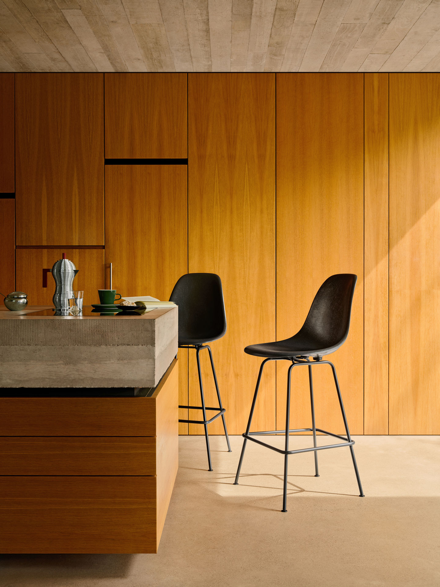 Zwei schwarze Eames Fiberglass Barhocker von Vitra mit Sitzpolster an einer Küchentheke aus Beton.
