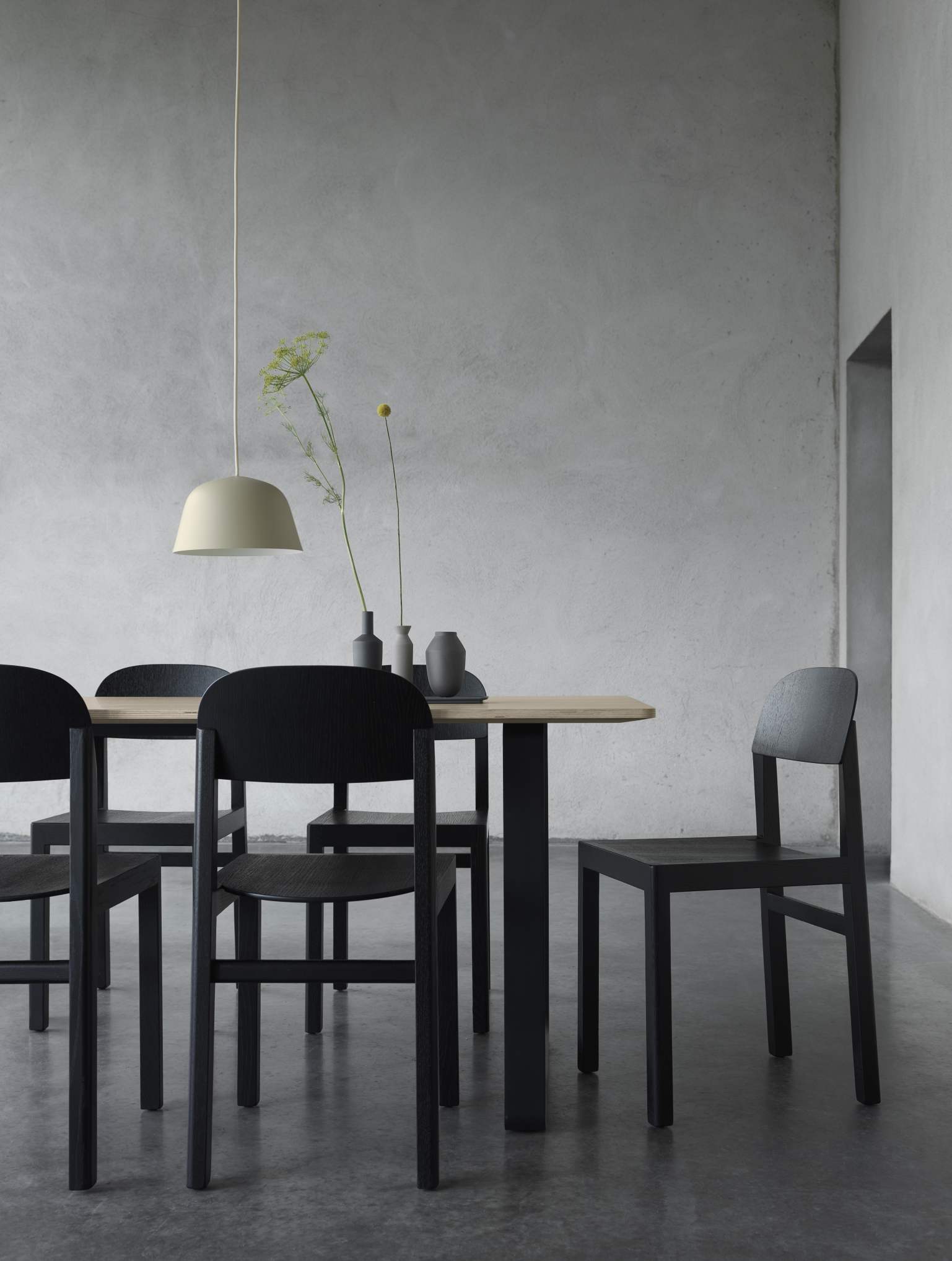 Helle Ambit Pendelleuchte von Muuto über Esstisch mit schwarzen Holzstühlen und minimalistischer Dekoration.