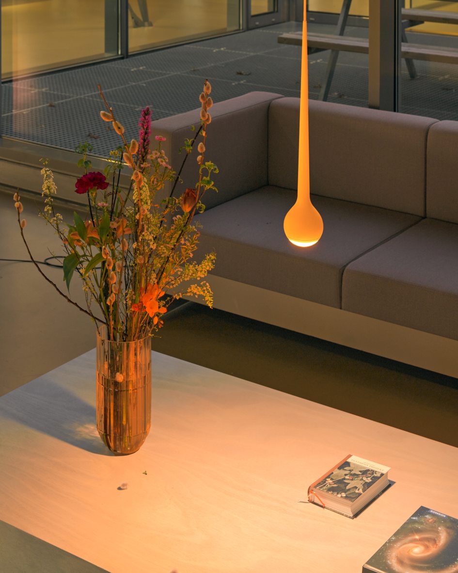Nahaufnahme der grauen Falling Sun Pendelleuchte über einem Couchtisch mit Blumen und Büchern.