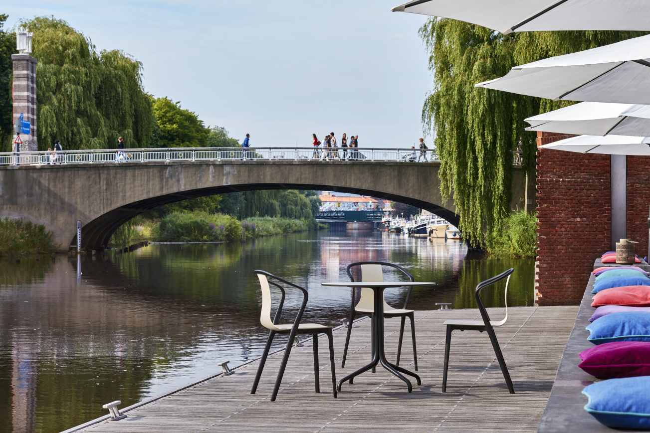 Vitra Belleville Table Tisch mit Stühlen am Flussufer unter einer Brücke, Außenbereich.