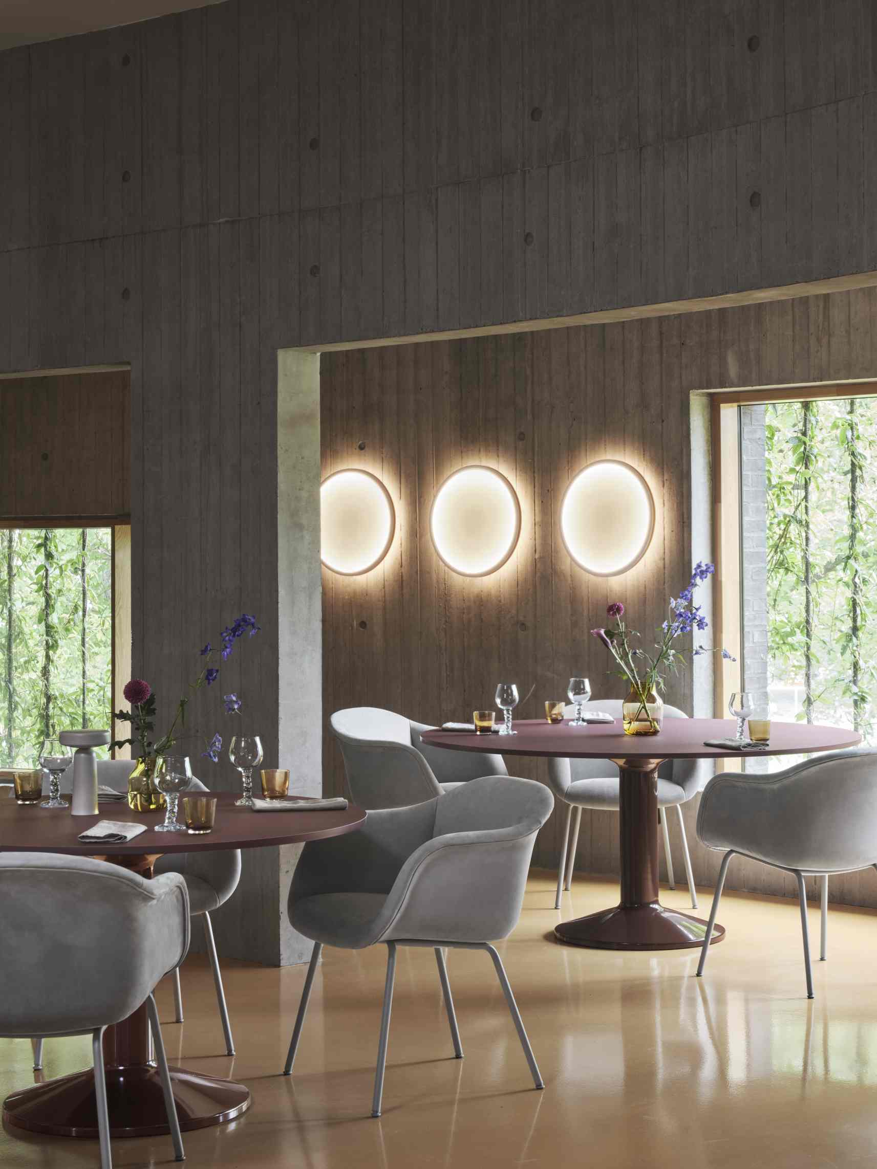 Ein grauer Fiber Soft Armchair von Muuto steht an einem gedeckten Esstisch.