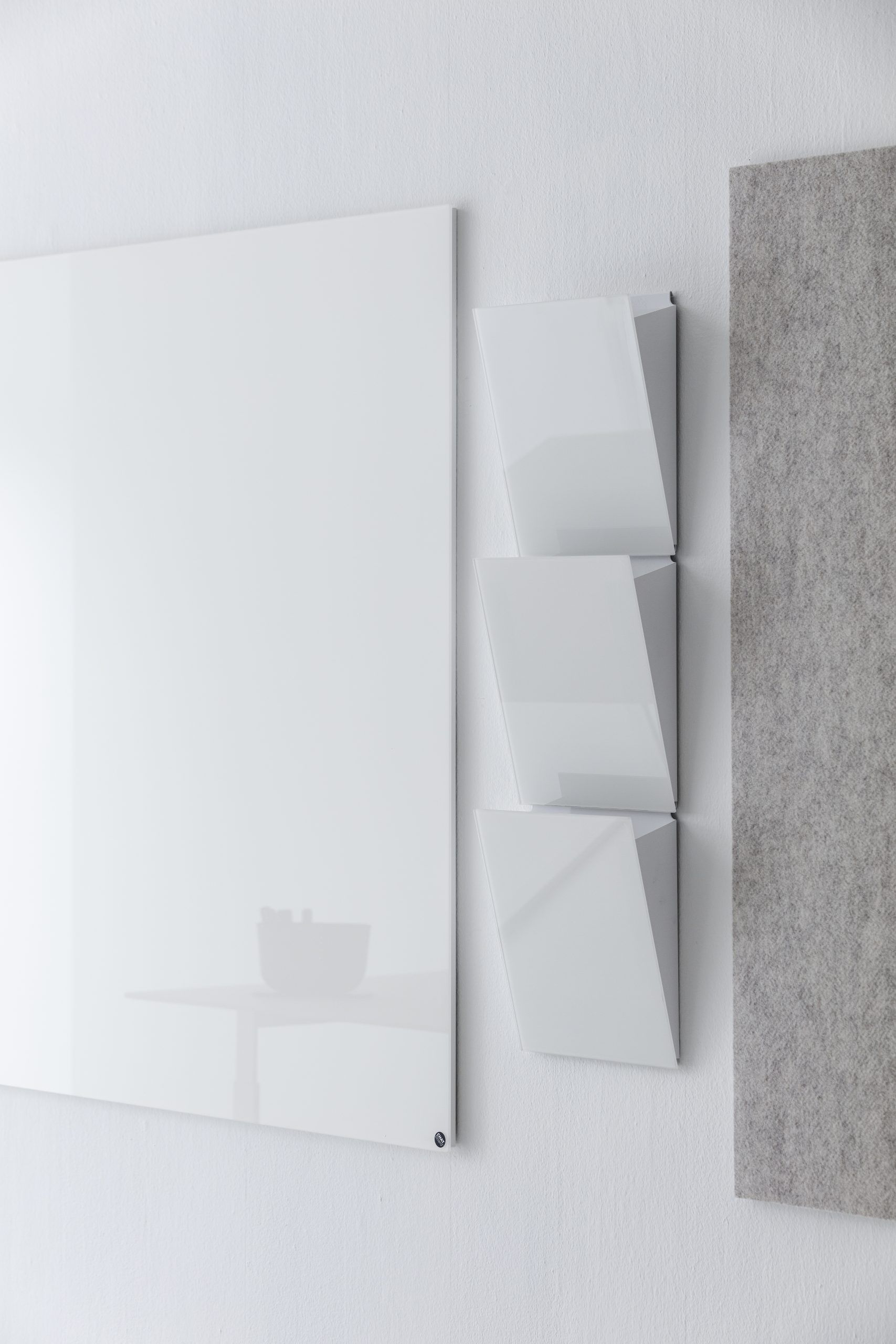 Chat Board Classic, weiße magnetische Glas-Wandtafel neben dreiteiliger, weißer Ablage und grauer Filzplatte an einer weißen Wand.