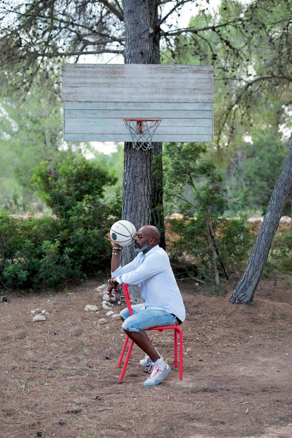 Mann sitzt auf rotem Luxembourg Outdoor Stuhl von Fermob unter Basketballkorb im Freien.