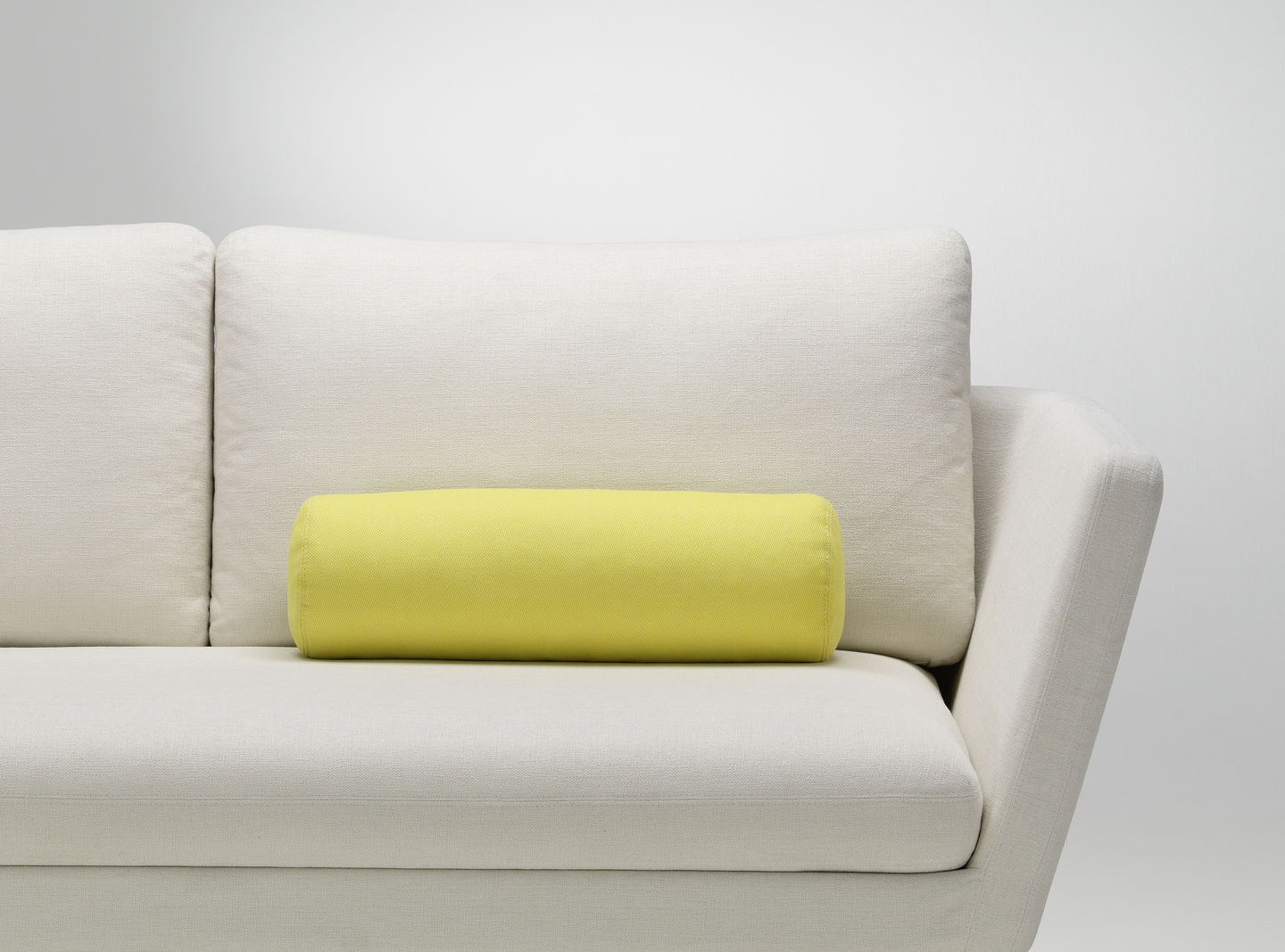 Vitra Cushions: Gelbes, zylinderförmiges Sofakissen auf einem weißen Sofa, modernes Wohnaccessoire für stilvolles Wohnzimmer.