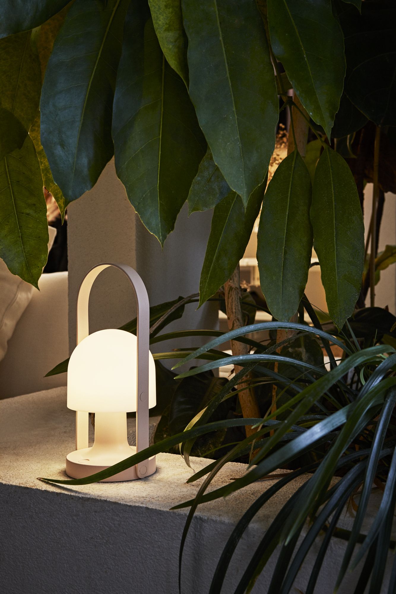 FollowMe LED Akku Tischleuchte von Marset, grüne tragbare Lampe mit warmem Licht, umgeben von Pflanzen.