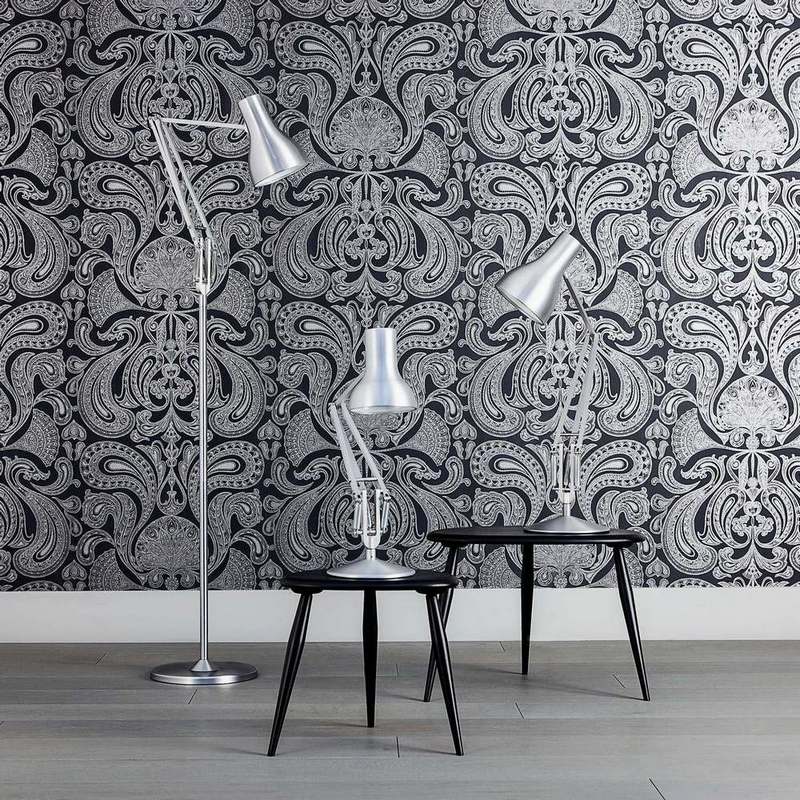 Anglepoise Type 75 Schreibtischleuchten: Stehleuchte und Tischleuchte in Silber auf schwarzen Tischen vor gemusterter Tapete.
