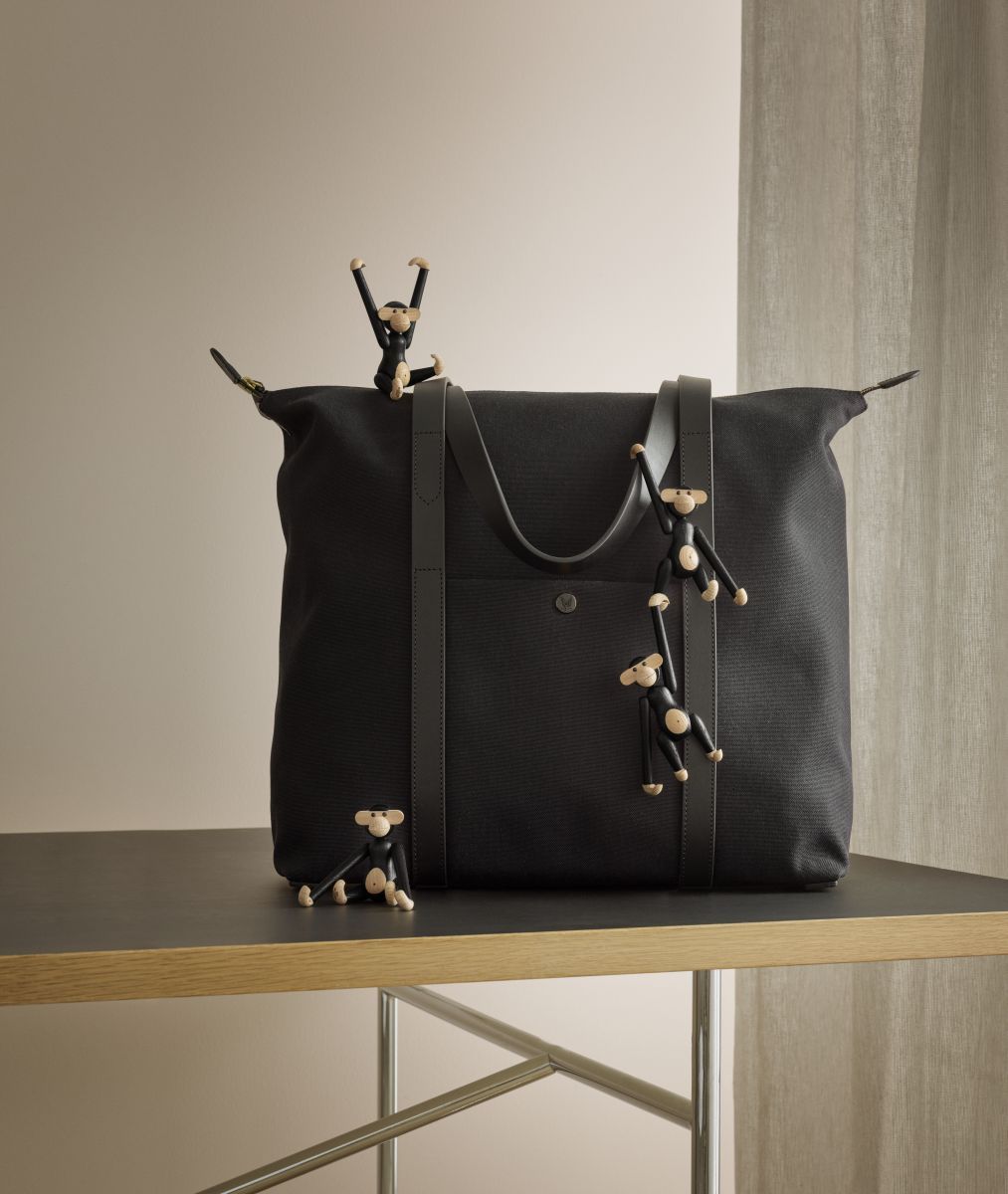 Kay Bojesen Affe Mini Holzfiguren auf einer schwarzen Tasche und einem Tisch arrangiert.