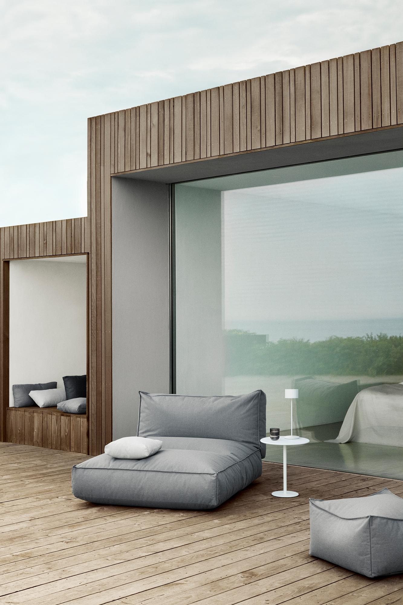 Graues STAY Kissen Outdoor von Blomus auf einer Holzterrasse mit Meerblick, minimalistisches Design.