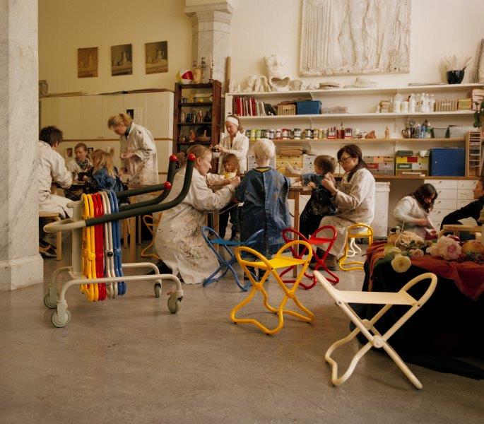Bunte Kinderhocker aus Metall in einem Atelier mit Kindern und Betreuern beim Basteln.