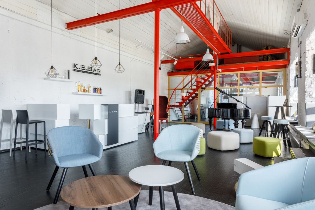 Innenaufnahme mit hellblauem ox:co Konferenzsessel Bejot, runden Tischen und Klavier in modernem Büro oder Lounge.