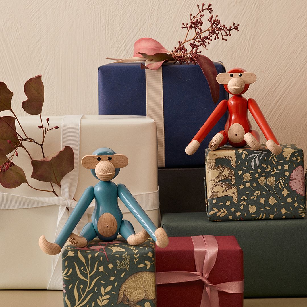 Buntes Stillleben mit zwei Kay Bojesen Mini Affen Holzfiguren in Rot und Blau auf Geschenkboxen.