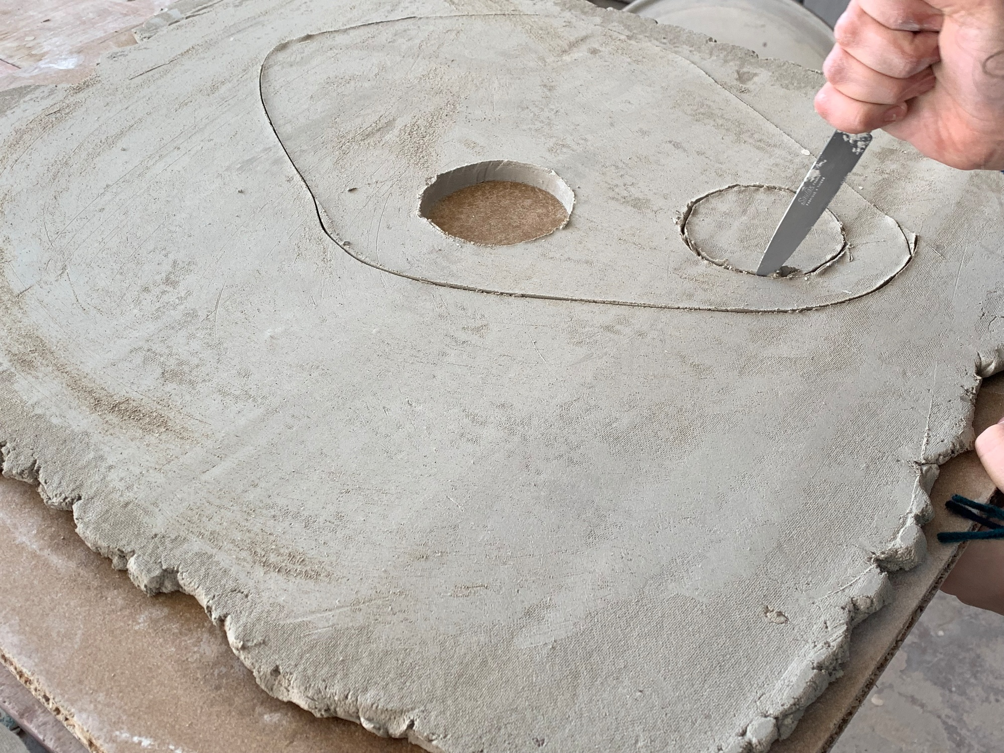 Nahaufnahme: Hand schneidet mit Werkzeug Löcher in Tonplatte für Vitra Découpage Vase.