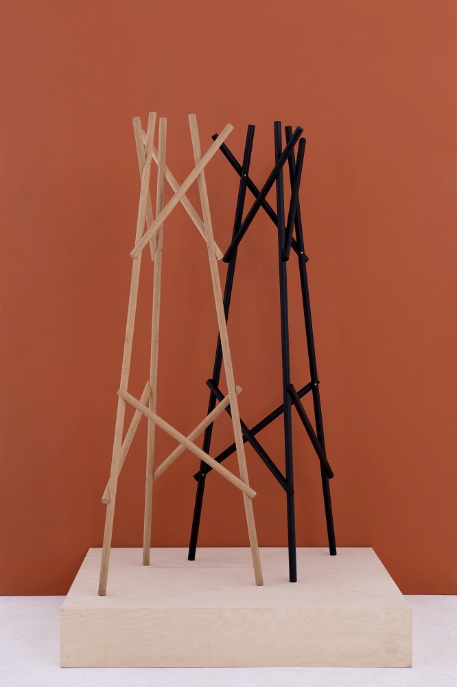 Kendo Garderobenständer von Cascando in Schwarz und Naturholz auf einem Holzpodest vor orangefarbenem Hintergrund.