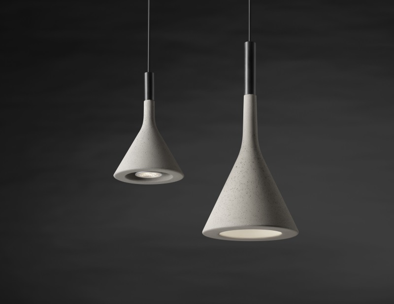 Zwei graue Aplomb Mini Pendelleuchten von Foscarini aus Beton vor dunklem Hintergrund.
