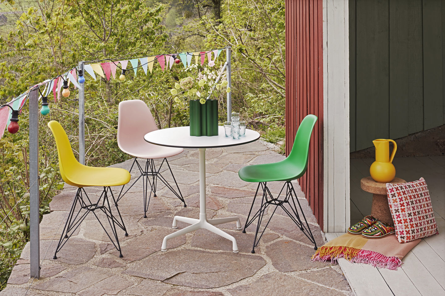 Drei Eames Plastic Side Chairs DSR in Gelb, Rosa und Grün um einen Tisch im Freien.