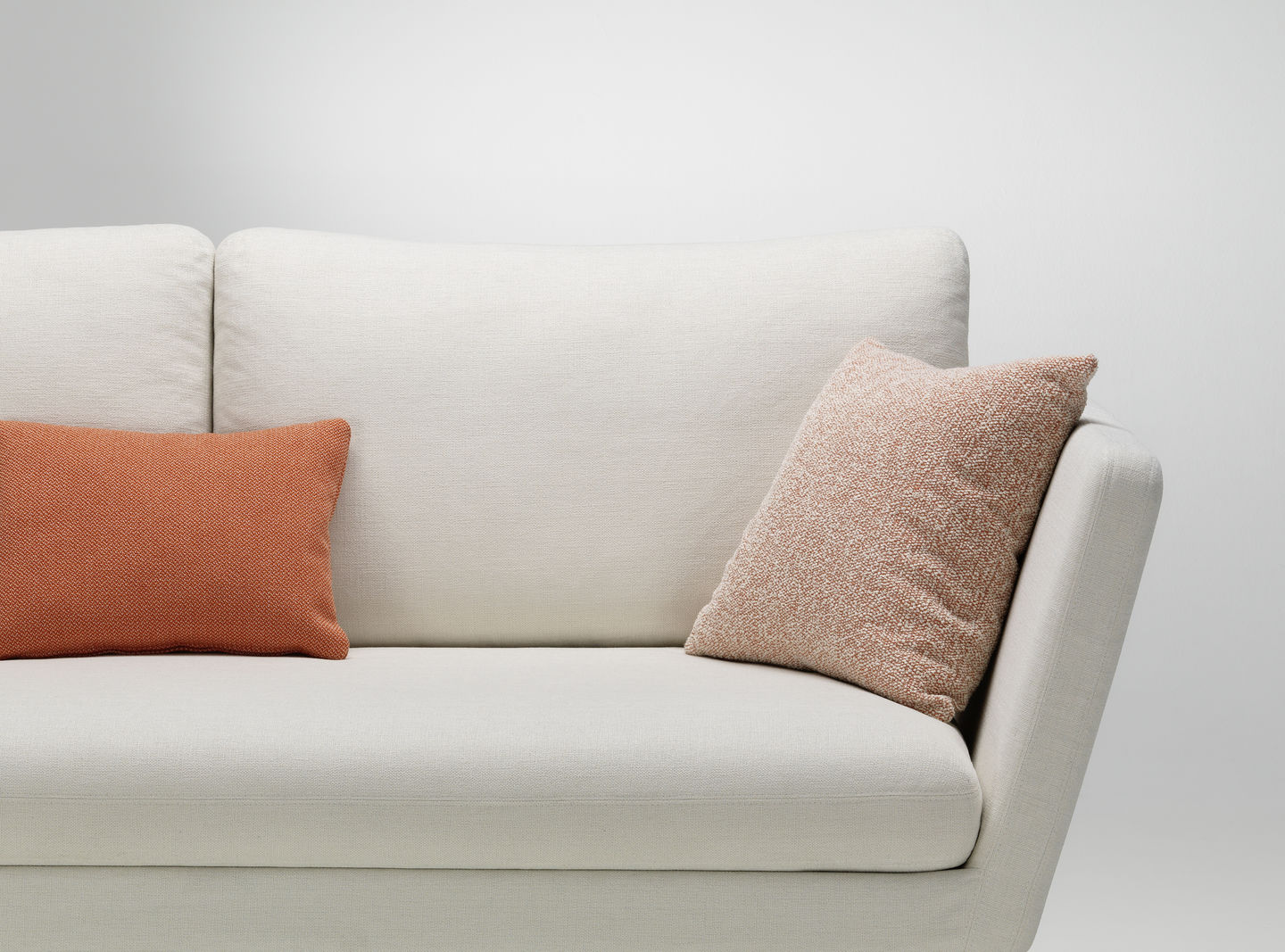 Vitra Kissen: Beigefarbenes Sofa mit einem orangefarbenen und einem gemusterten Sofakissen in Terrakotta.