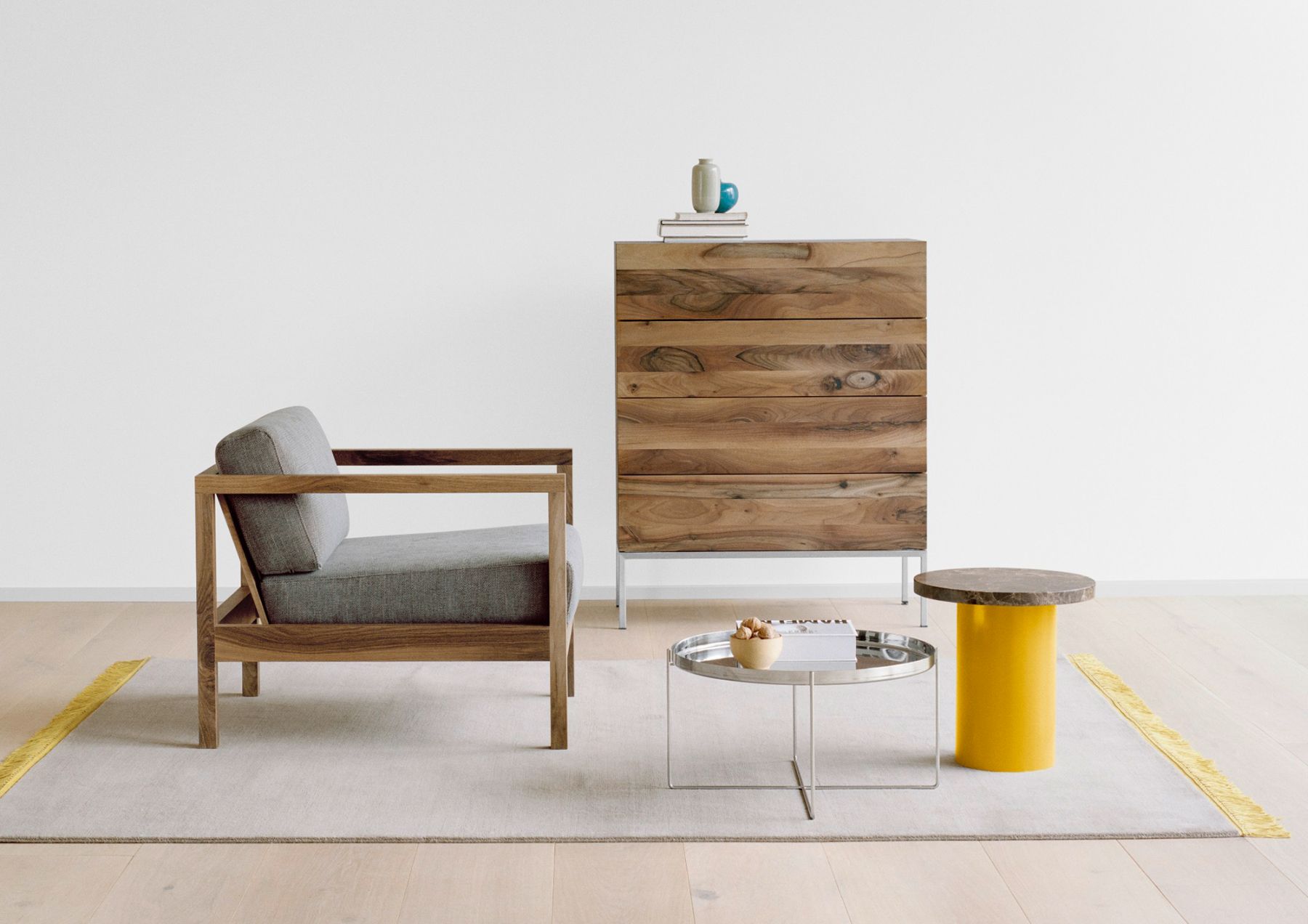 Gelber Enoki Beistelltisch von e15 neben Sessel und Kommode in minimalistischem Wohnzimmer.