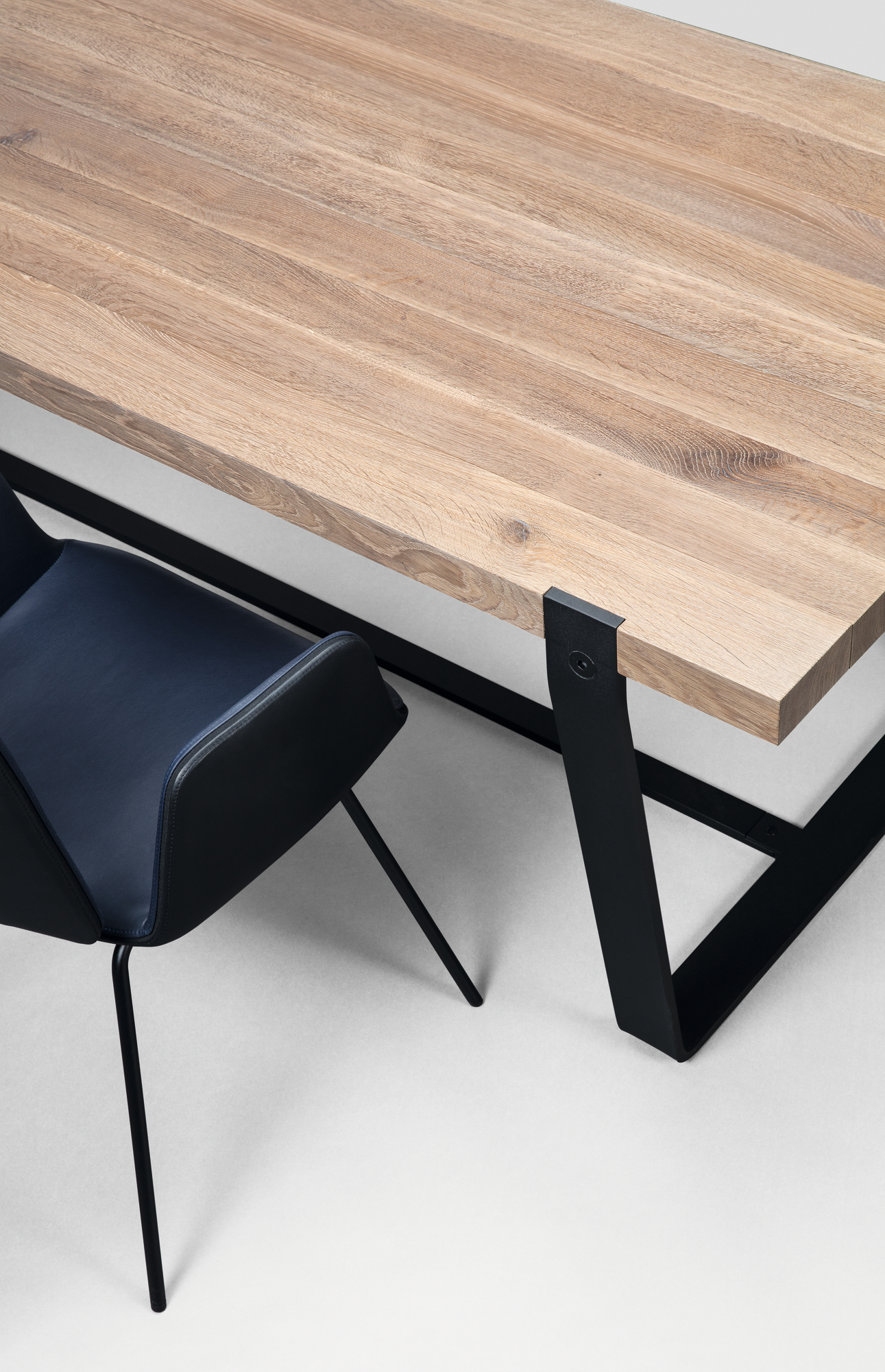 Detailaufnahme von Janua BB 11 Clamp Tisch mit Eichenholzplatte und schwarzem Metallgestell, dazu ein blauer Stuhl.