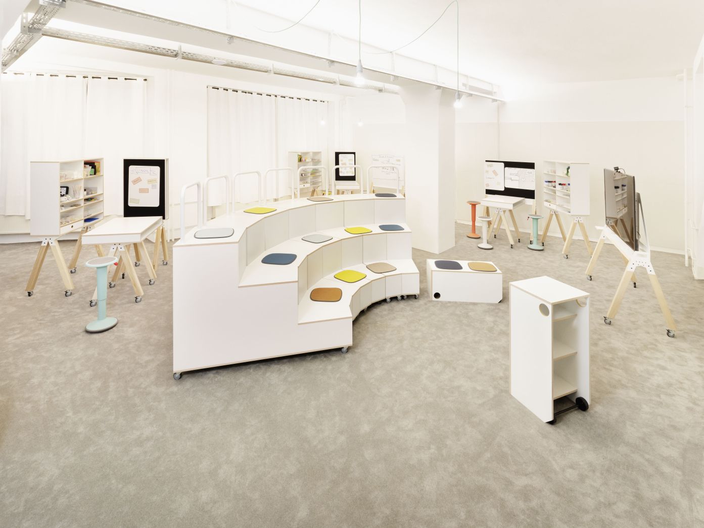 What if We Fly Taskboard Medienwand mit Whiteboard, Hocker und Stauraumelementen in hellem Raum.