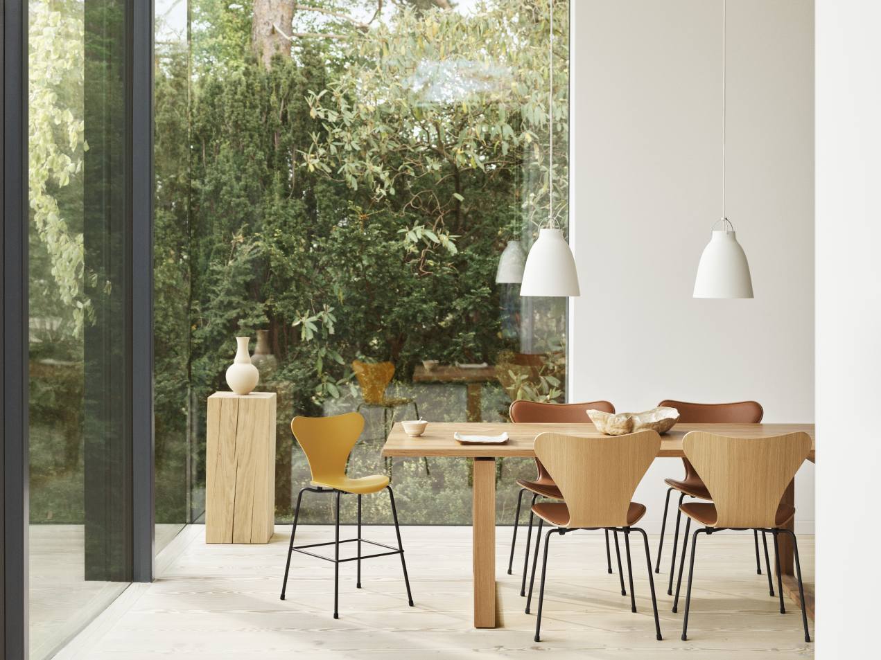 Esszimmer mit Holztisch, Stühlen und zwei weißen Caravaggio Pendelleuchten von Fritz Hansen über dem Tisch.