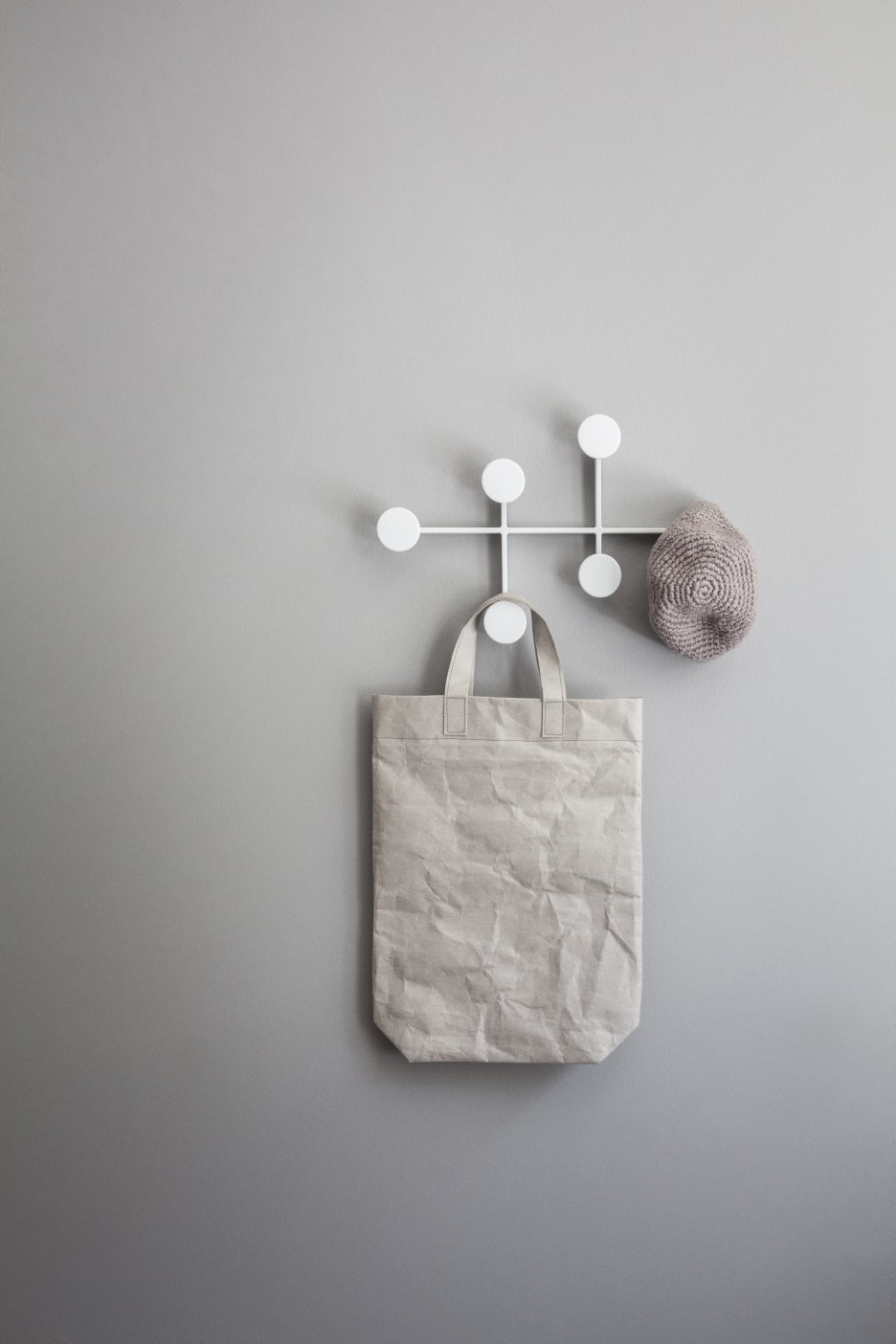 Afteroom Coat Hanger Medium: Weiße Garderobe mit Tasche und Mütze an grauer Wand.