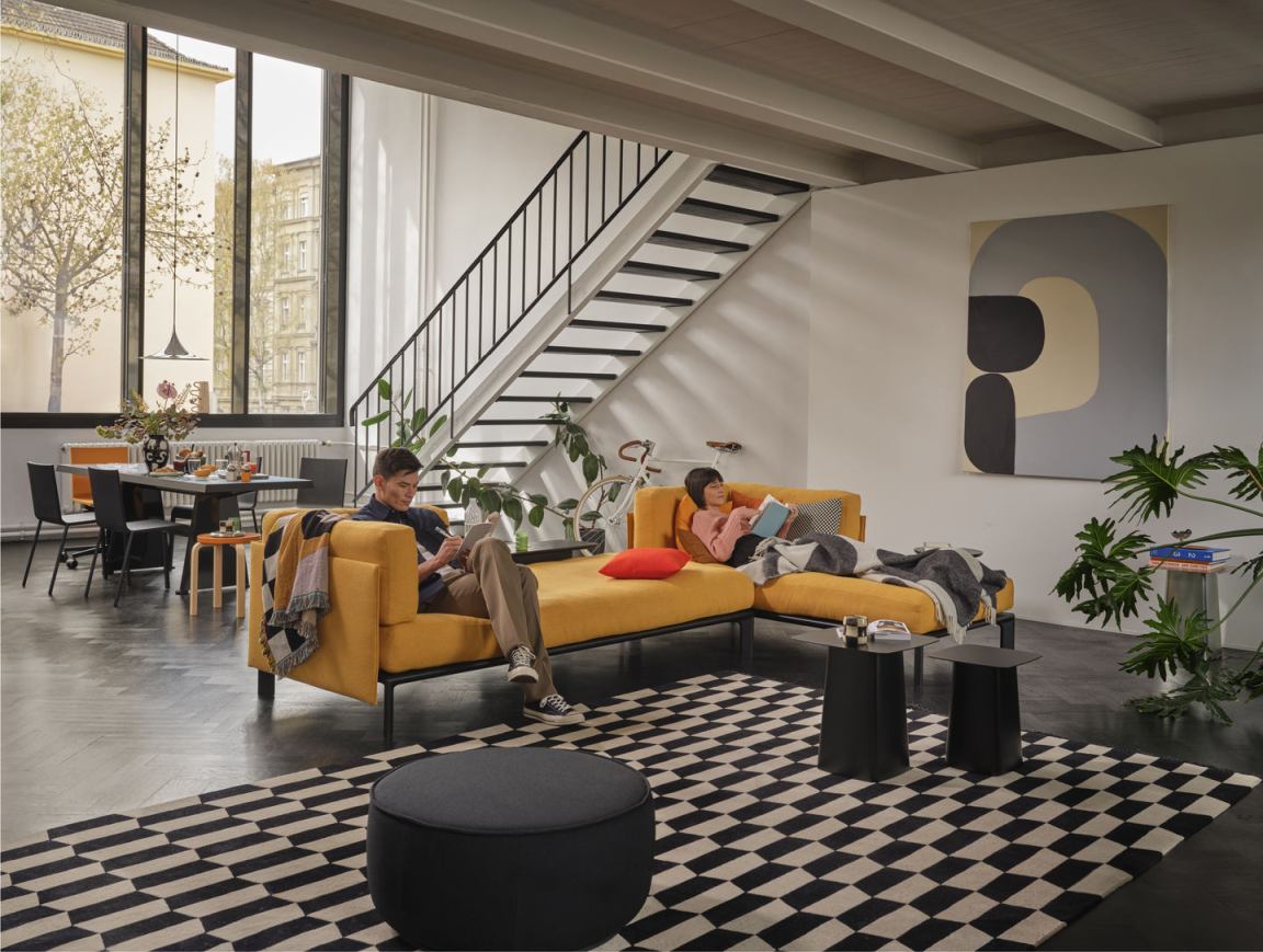 Helles Wohnzimmer mit gelbem Anagram Rücken- und Seitenkissen von Vitra, zwei Personen entspannen auf dem Sofa.