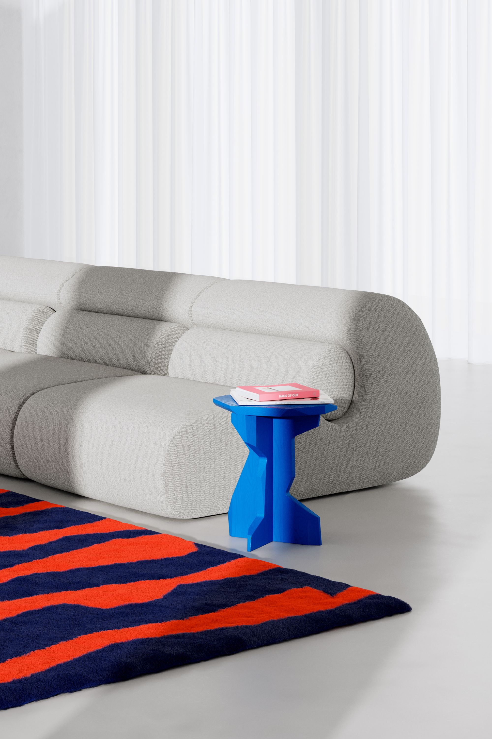 OLA Sofa mit blauem Hocker und Teppich mit Streifenmuster in einem hellen, modernen Wohnzimmer.