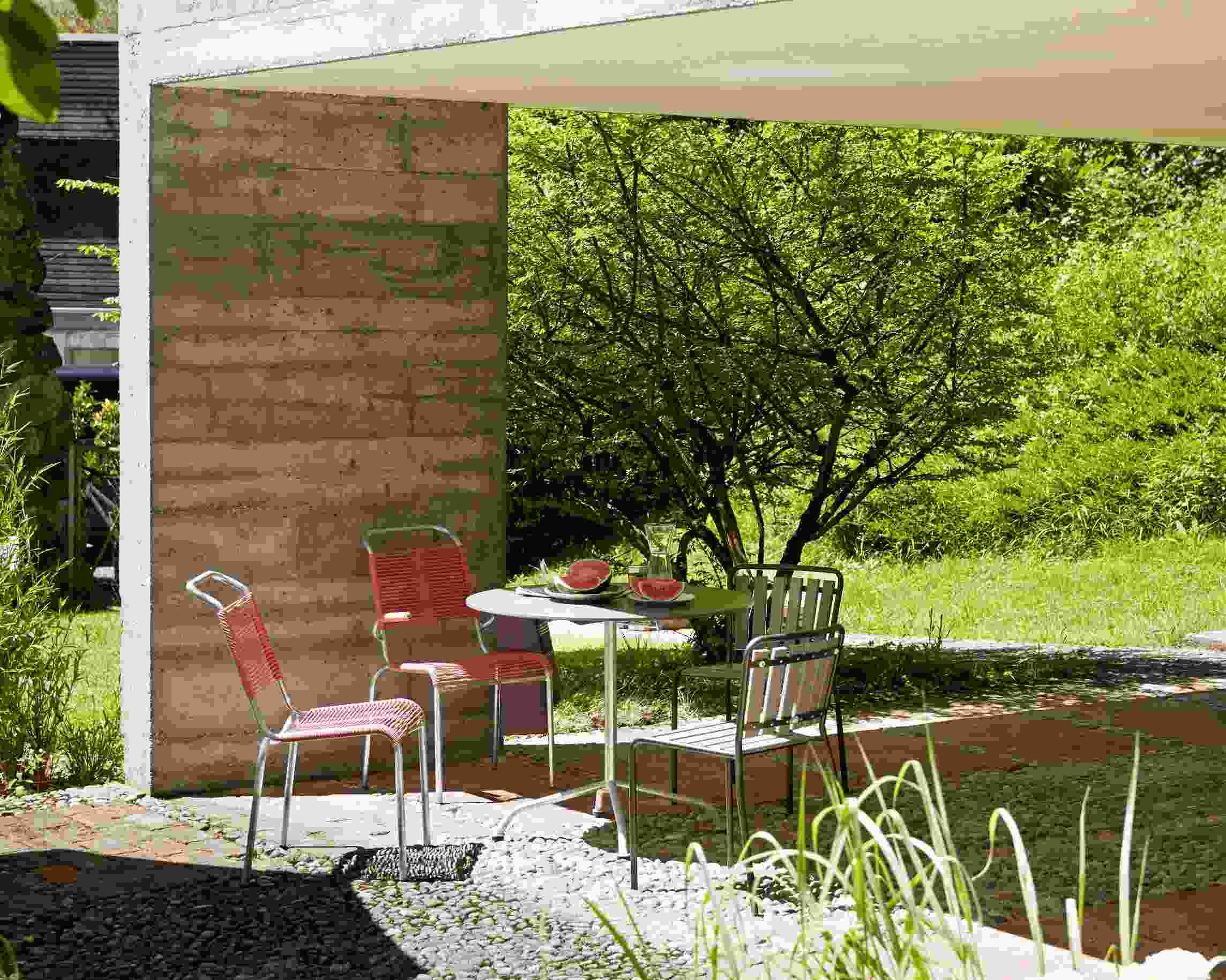 Feuerroter Haefeli Stuhl Outdoor mit Tisch und Wassermelone im Garten. Design Gartenmöbel.