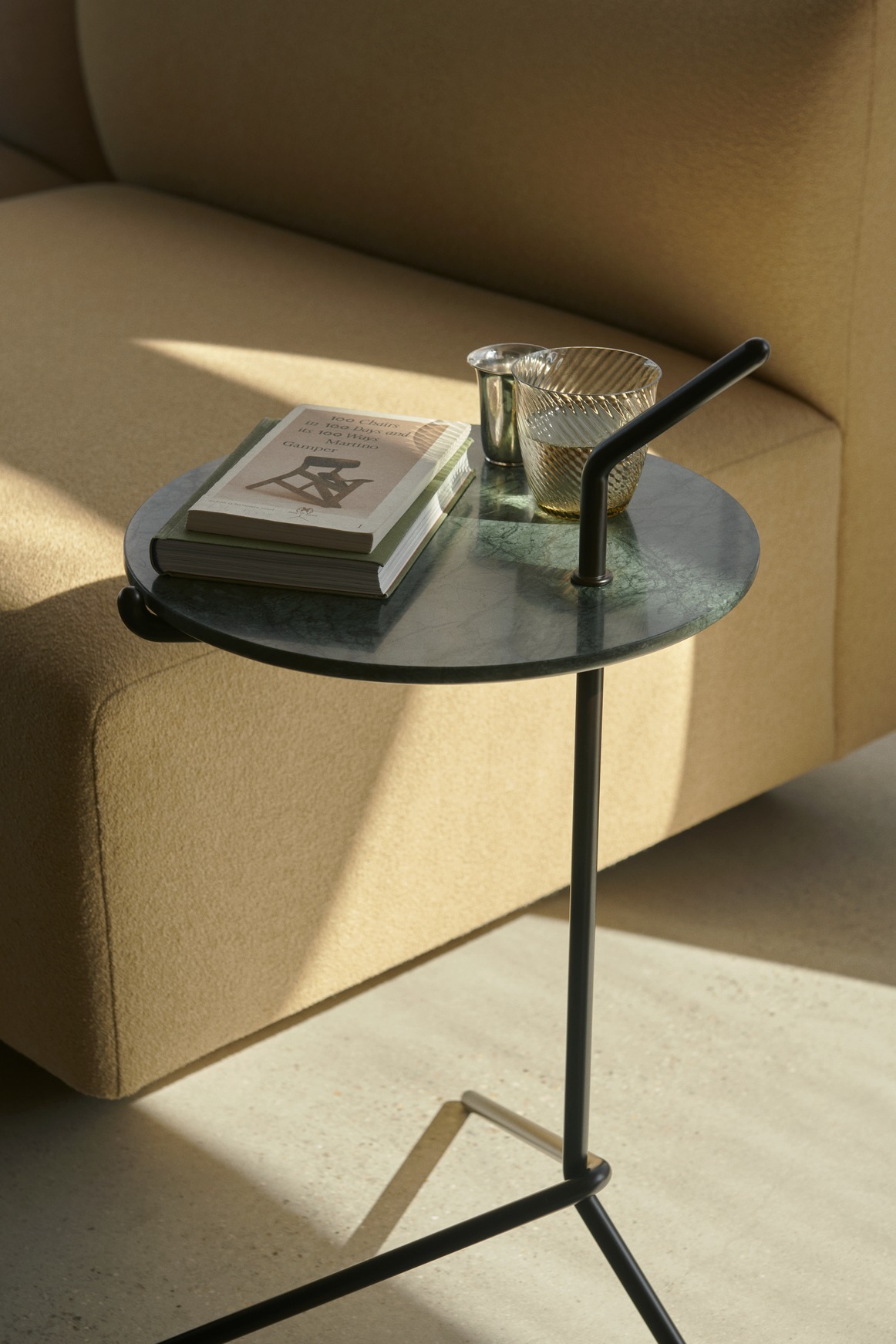AndTradition Halten SH9 Beistelltisch mit grüner Marmorplatte, Buch und Glas neben beigem Sofa.