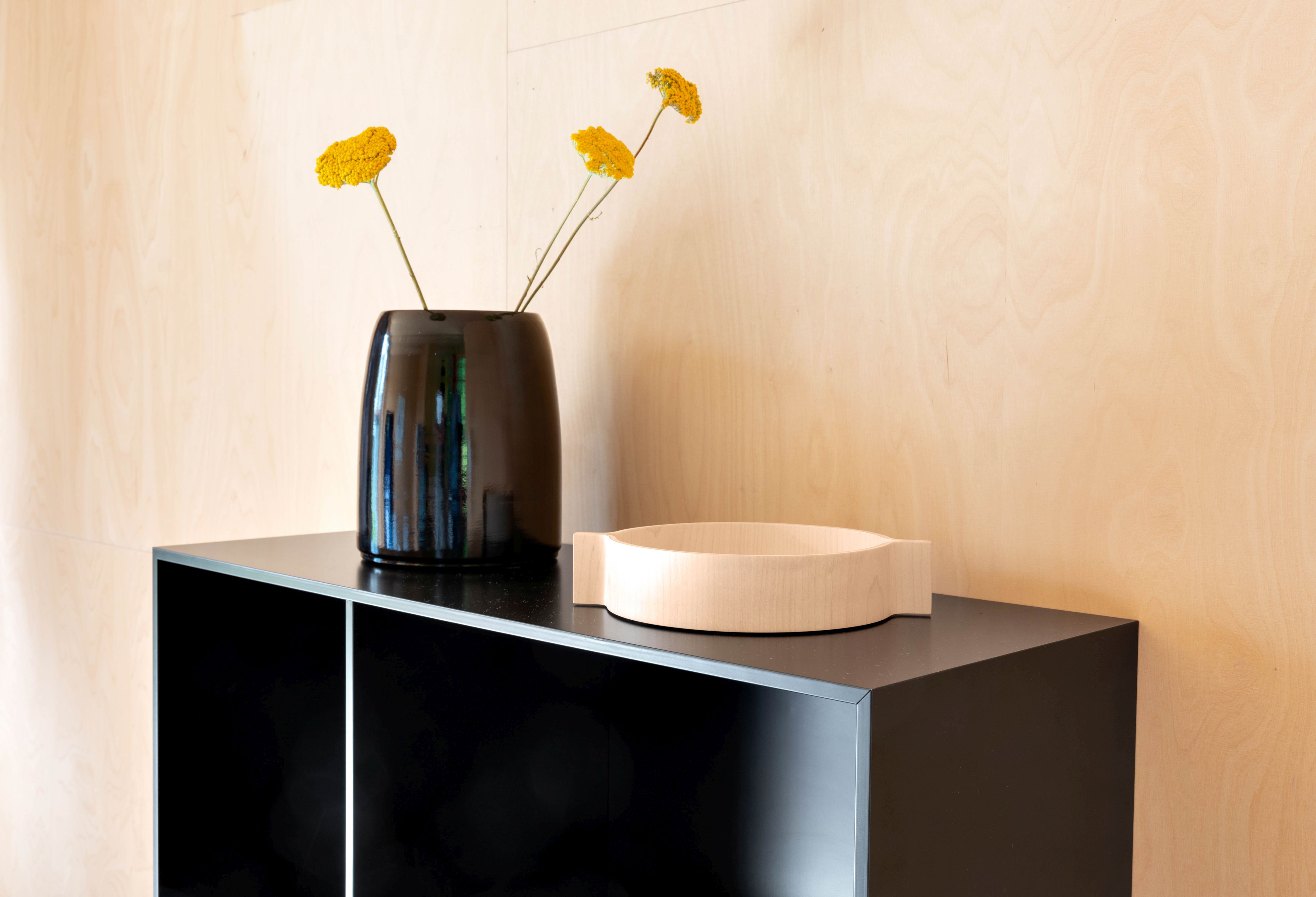Schwarze Carla Vase von Schönbuch mit gelben Blumen auf einem schwarzen Sideboard. Dekorative Wohnaccessoires.