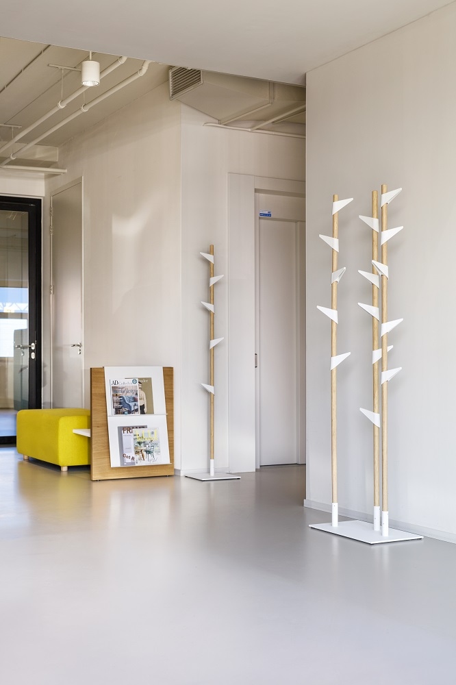 Cascando Bamboo Standgarderobe aus Holz mit weißen Haken in einem modernen Büroflur.