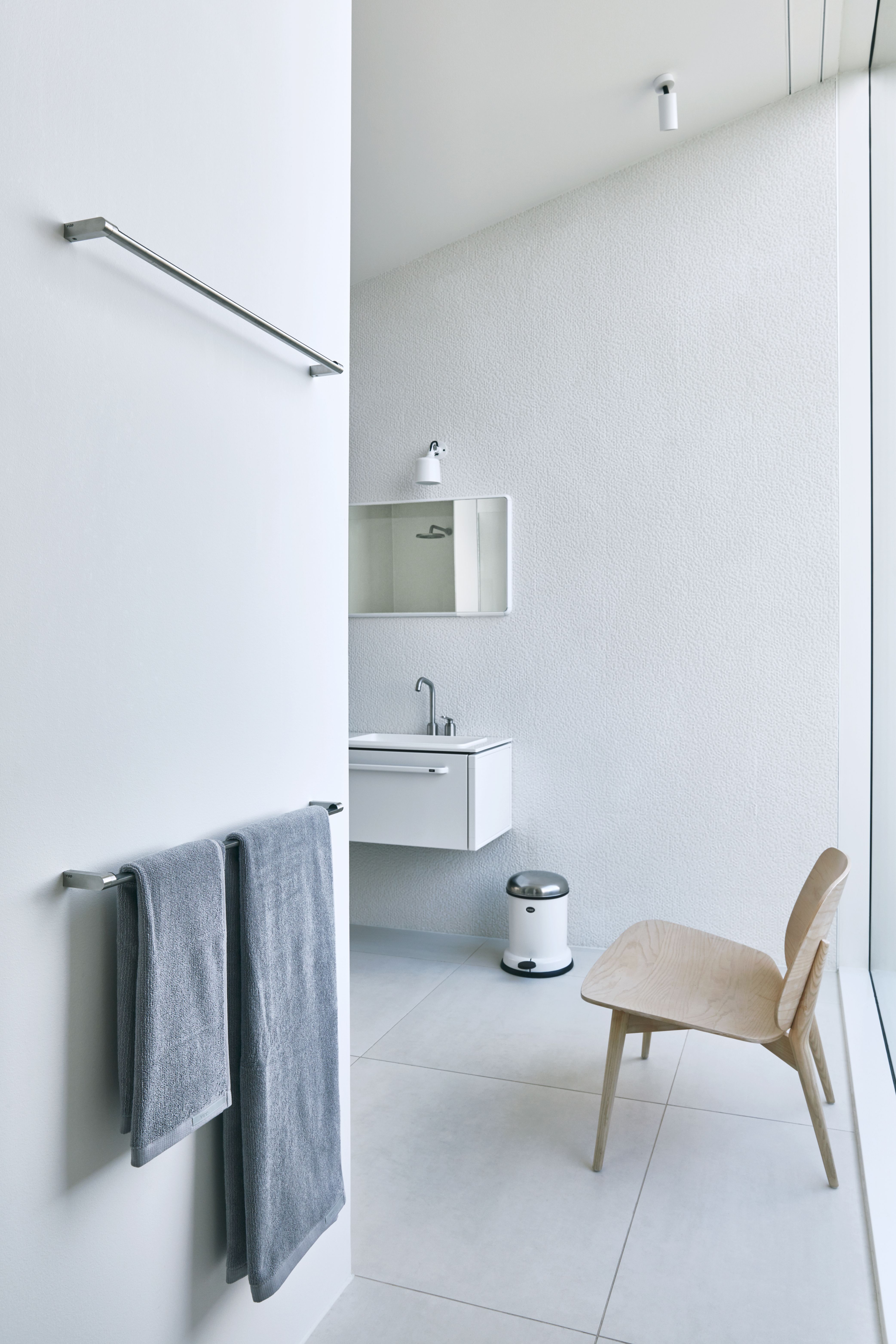 Helles Badezimmer mit Vipp Handtuchstange aus Edelstahl, an der zwei graue Handtücher hängen.