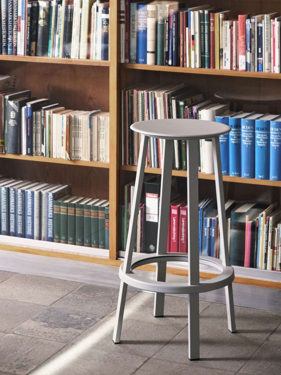 Grauer Revolver Bar Stool Barhocker High Hay vor einem Bücherregal, modernes Design für Küche oder Bar.