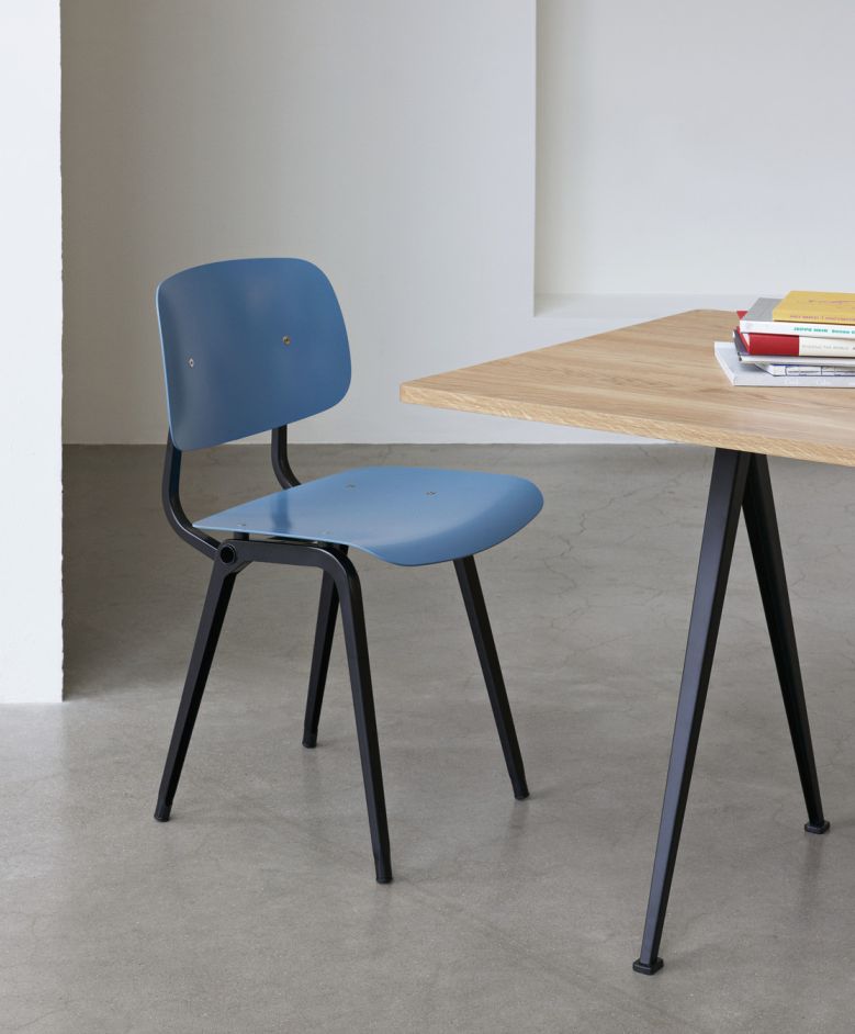 Blauer Hay Revolt Chair Stuhl mit schwarzem Gestell neben einem Holztisch im minimalistischen Design.