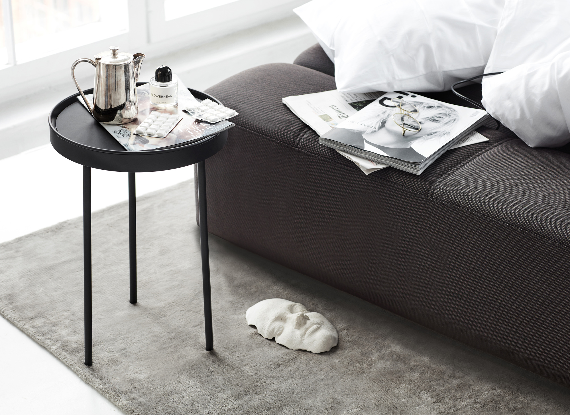 Graues Daybe Schlafsofa mit Kissen, Beistelltisch, Teekanne und Dekoration in modernem Wohnzimmer.