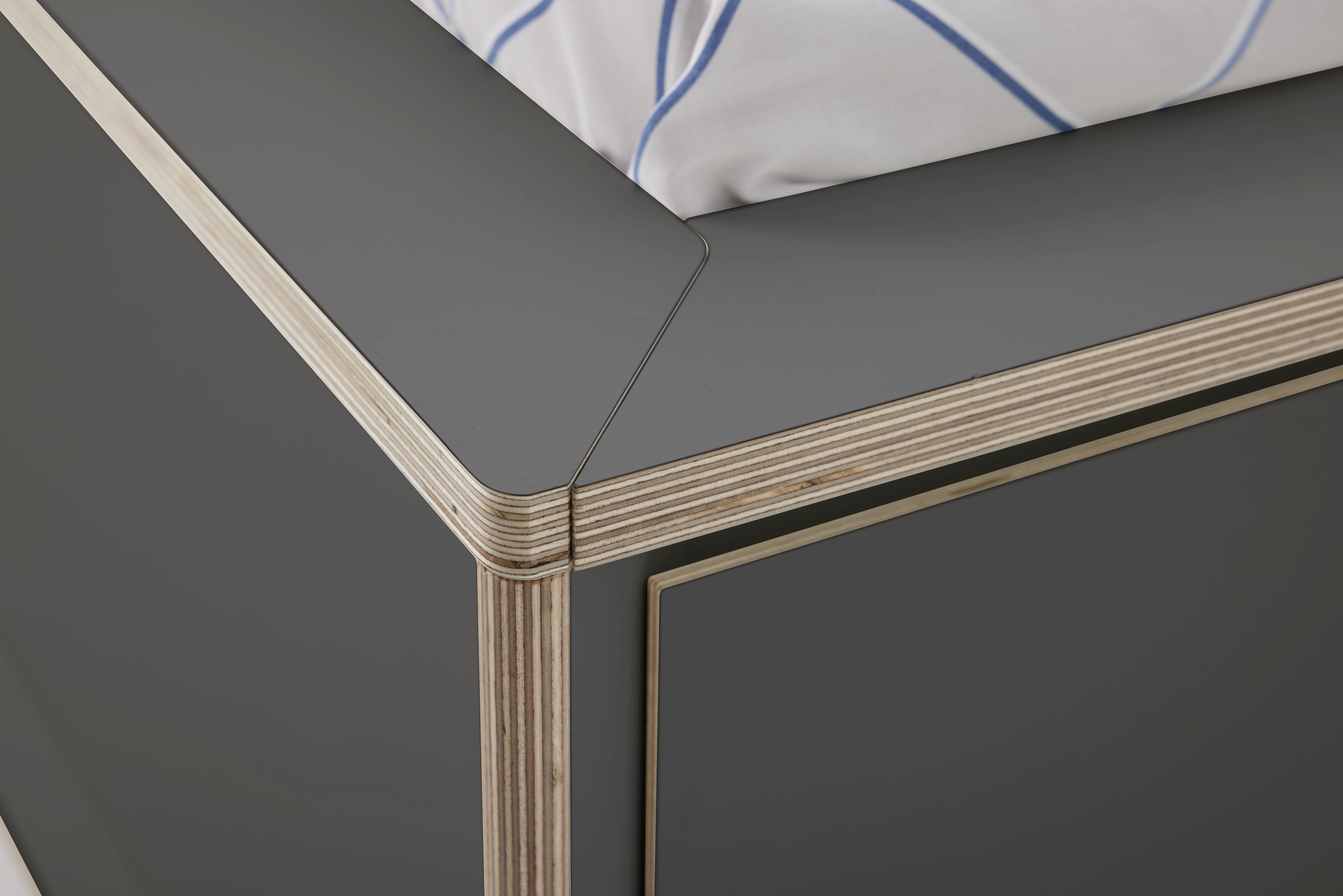 Detailaufnahme vom grauen Spaze Bett von Müller Möbelwerkstätten mit Bettwäsche und markanter Holzstruktur.