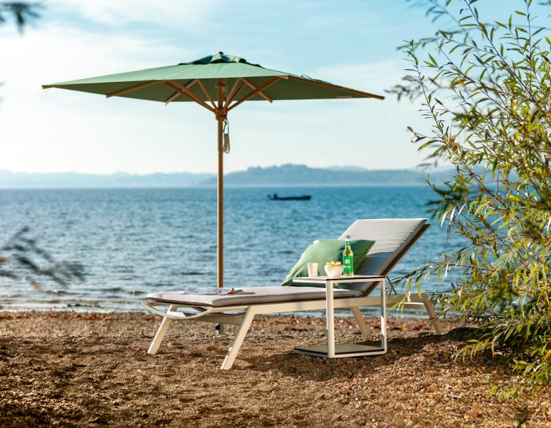 Weishäupl Klassiker Sonnenschirm über einer Sonnenliege am Strand mit Meerblick für entspannte Sommertage.