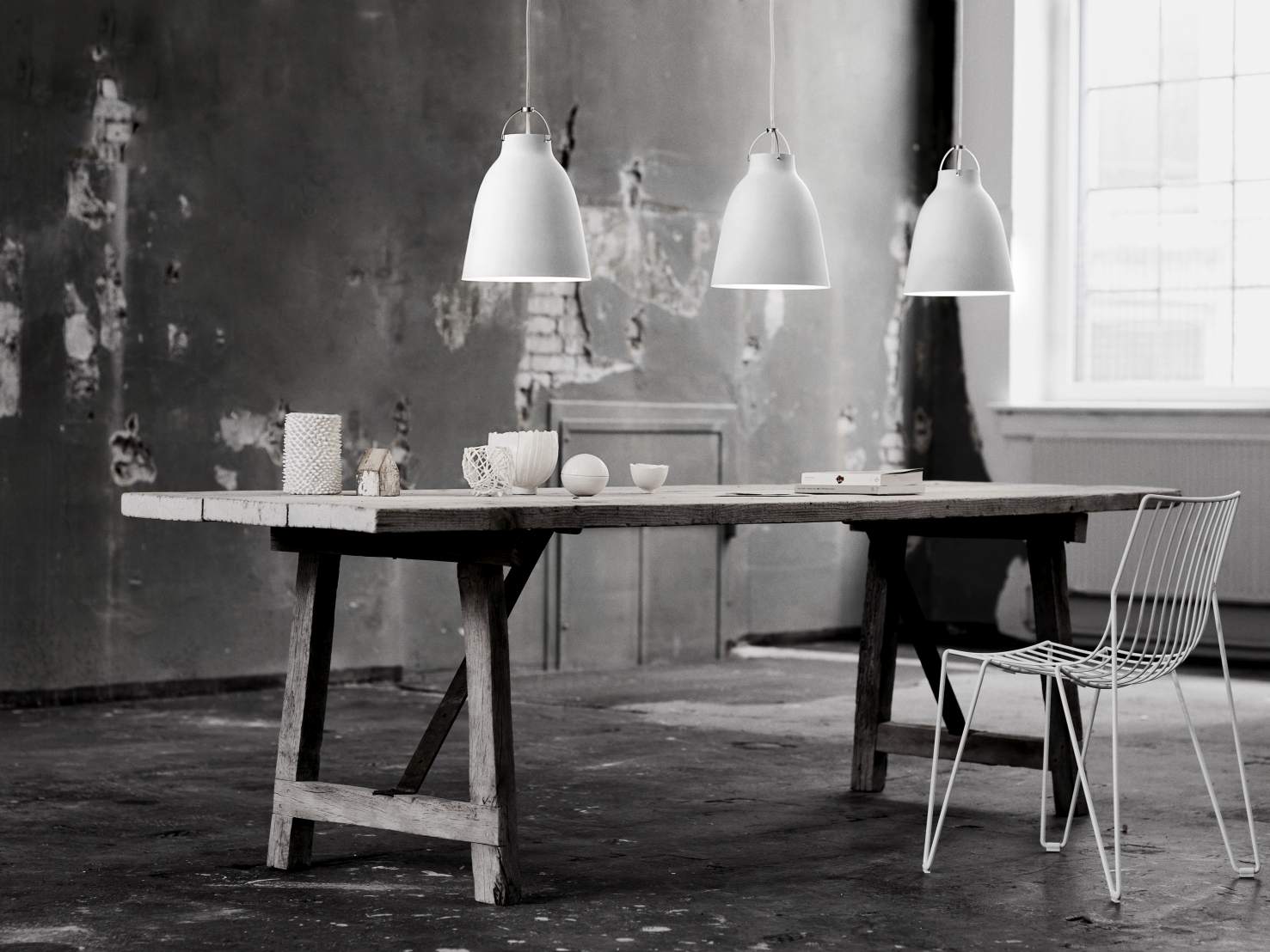Drei weiße Caravaggio Pendelleuchten von Fritz Hansen hängen über einem Tisch in einem minimalistischen Raum.