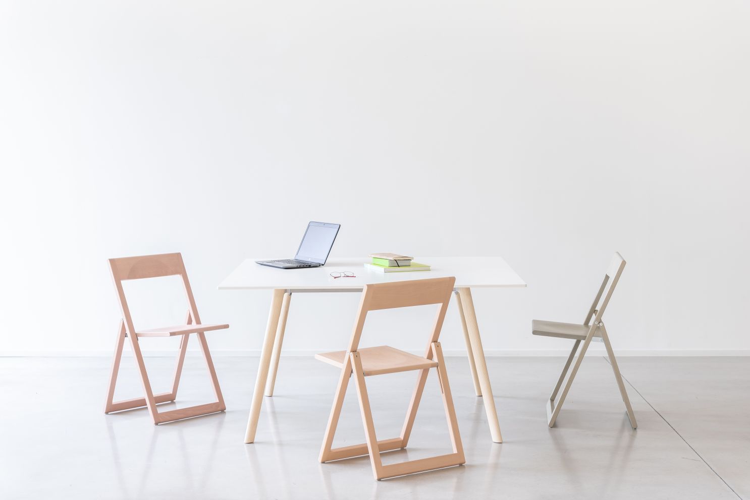 Weißer Pilo Tisch von Magis mit Laptop, Büchern und drei Holzstühlen in minimalistischem Büro.