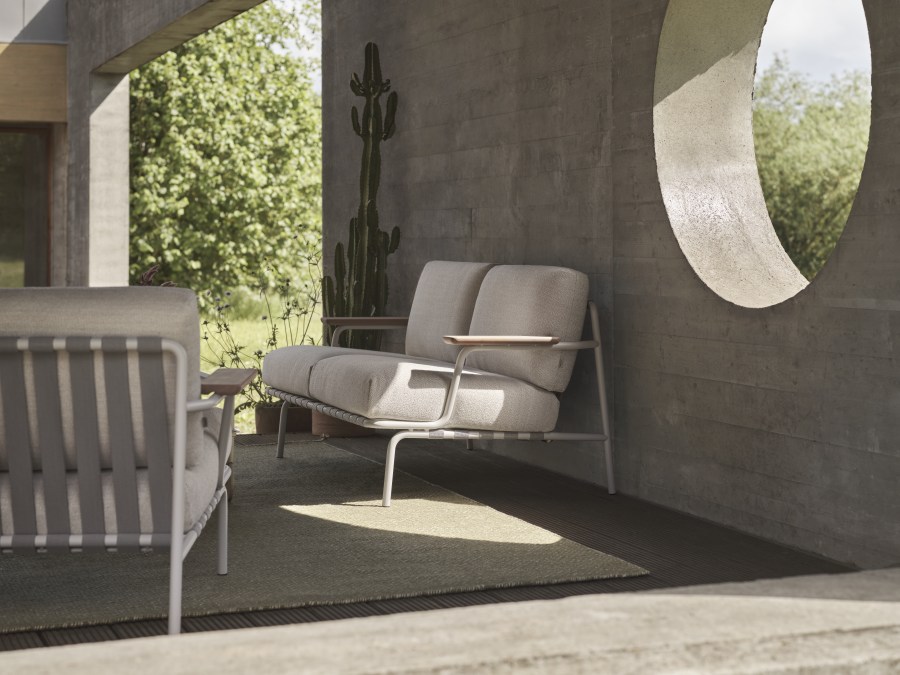 Muuto Settle Lounge Chair Outdoor Sessel mit hellgrauem Stoffbezug und filigranem Metallgestell auf Terrasse.