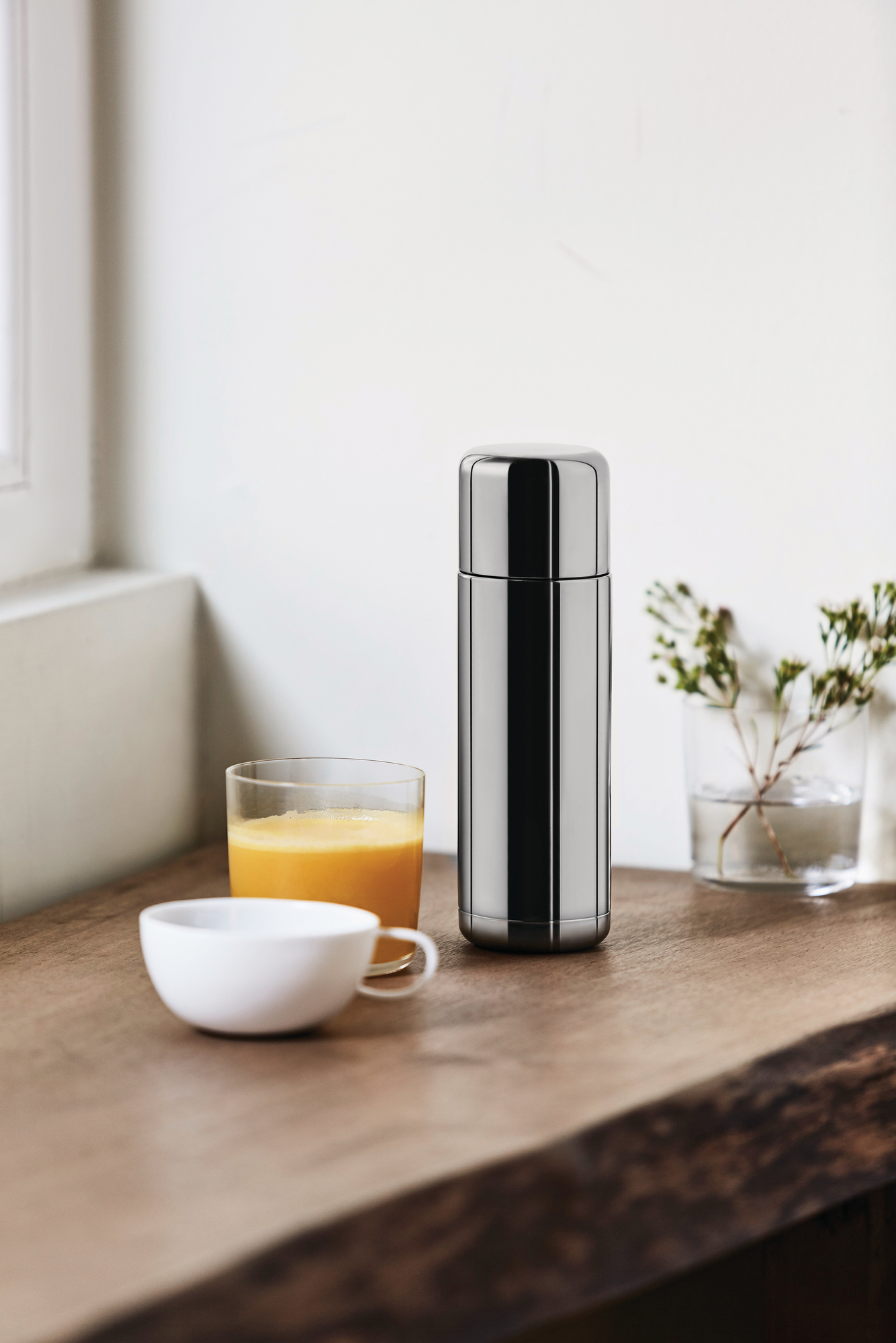 Nahaufnahme der Nomu Isolierkanne von Alessi, aus Edelstahl, neben Saft und Tasse.