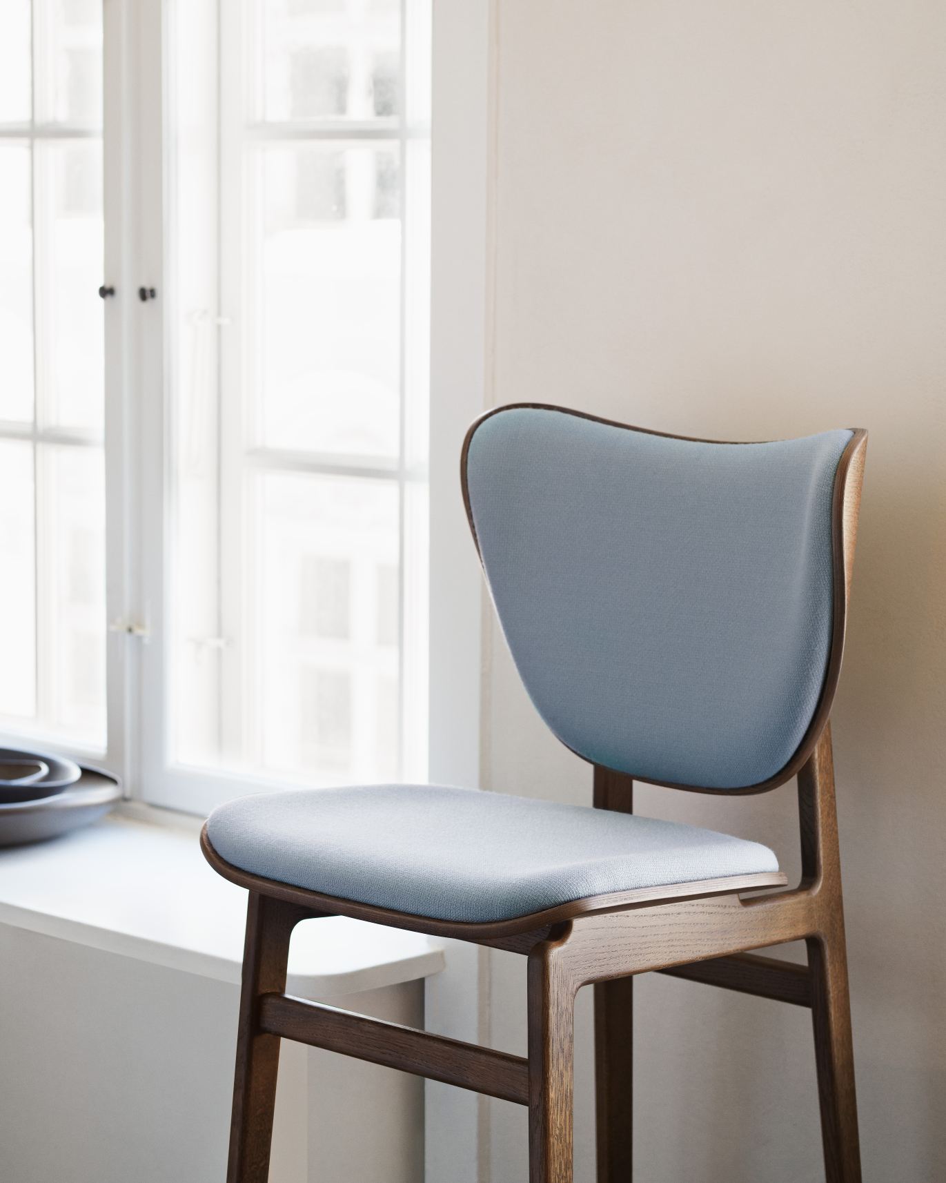 Nahaufnahme des NORR11 Elephant Dining Chair Stuhls mit blauer Polsterung und dunklem Holzrahmen.