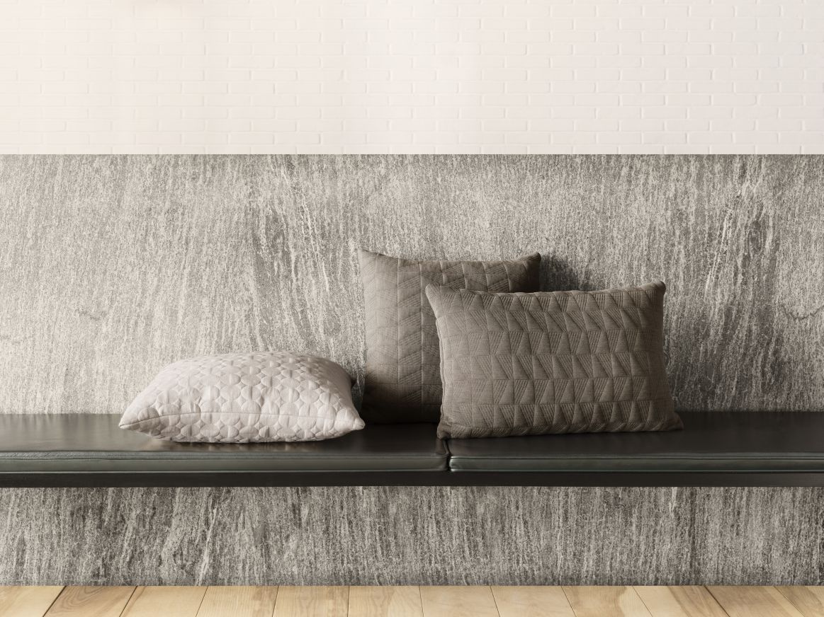 Drei dekorative Kissen, darunter ein Vertigo Arne Jacobsen Kissen in Sand, auf einer Bank.