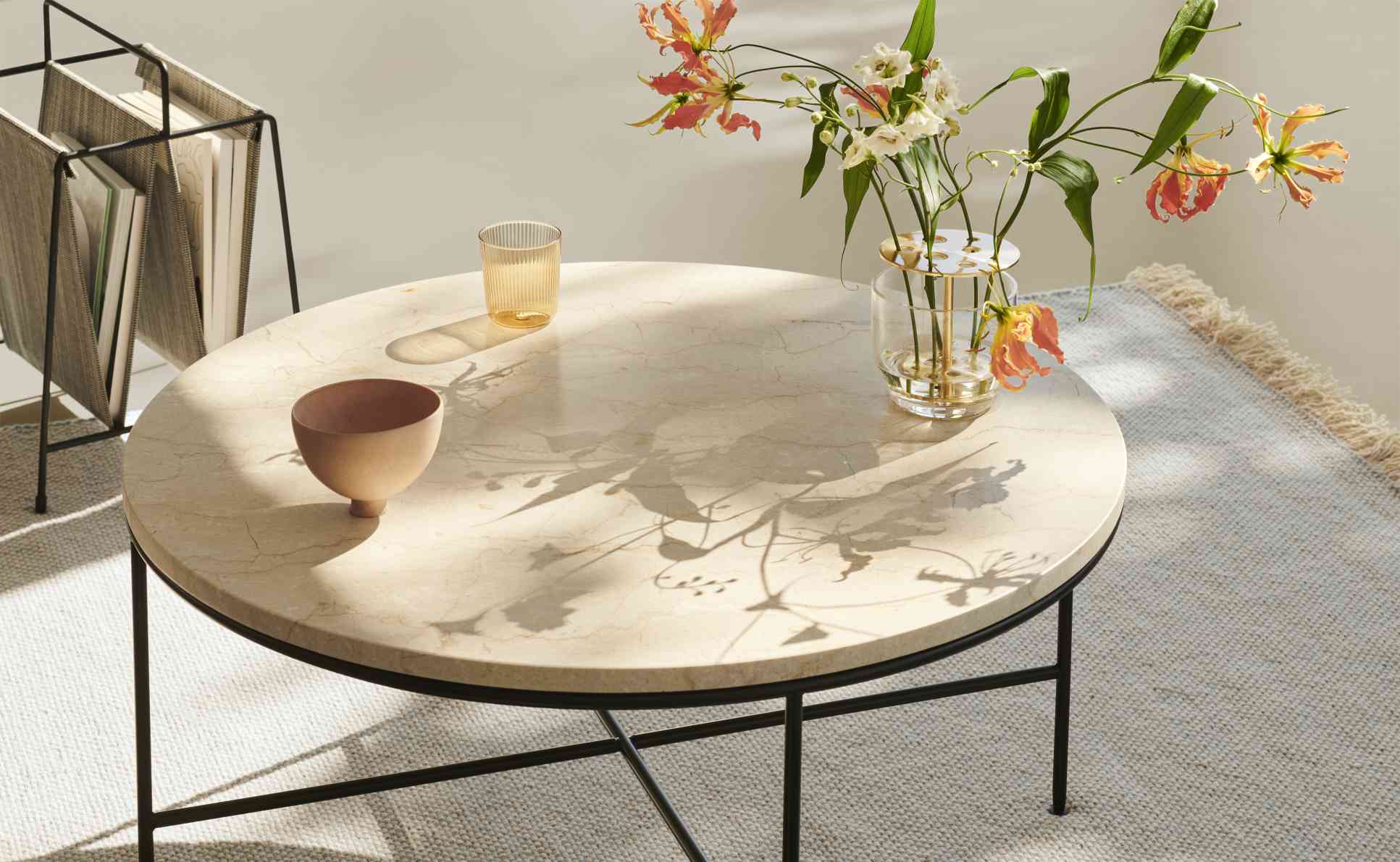 Fritz Hansen Planner Couchtisch aus Marmor mit Blumen, Schale und Glas auf einem Teppich.