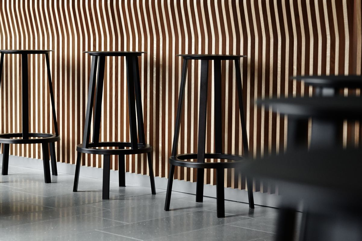 Schwarze Revolver Barhocker von Hay, minimalistisches Design für Küche oder Bar mit Holzpaneelwand im Hintergrund.