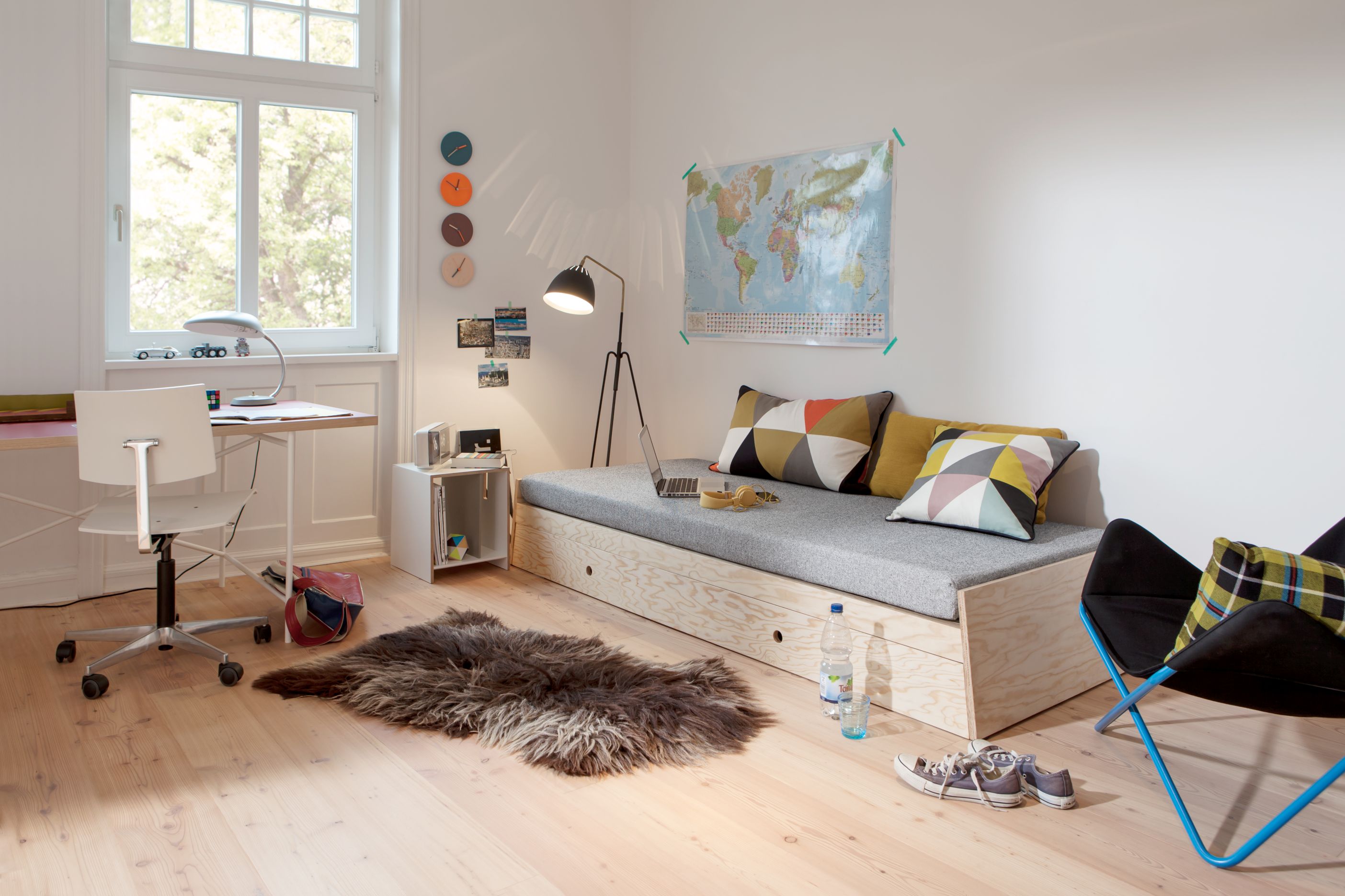 Helles Kinderzimmer mit Holz-Tagesbett, Schreibtisch, Schaffellteppich und Weltkarte für inspirierende Einrichtungsideen.
