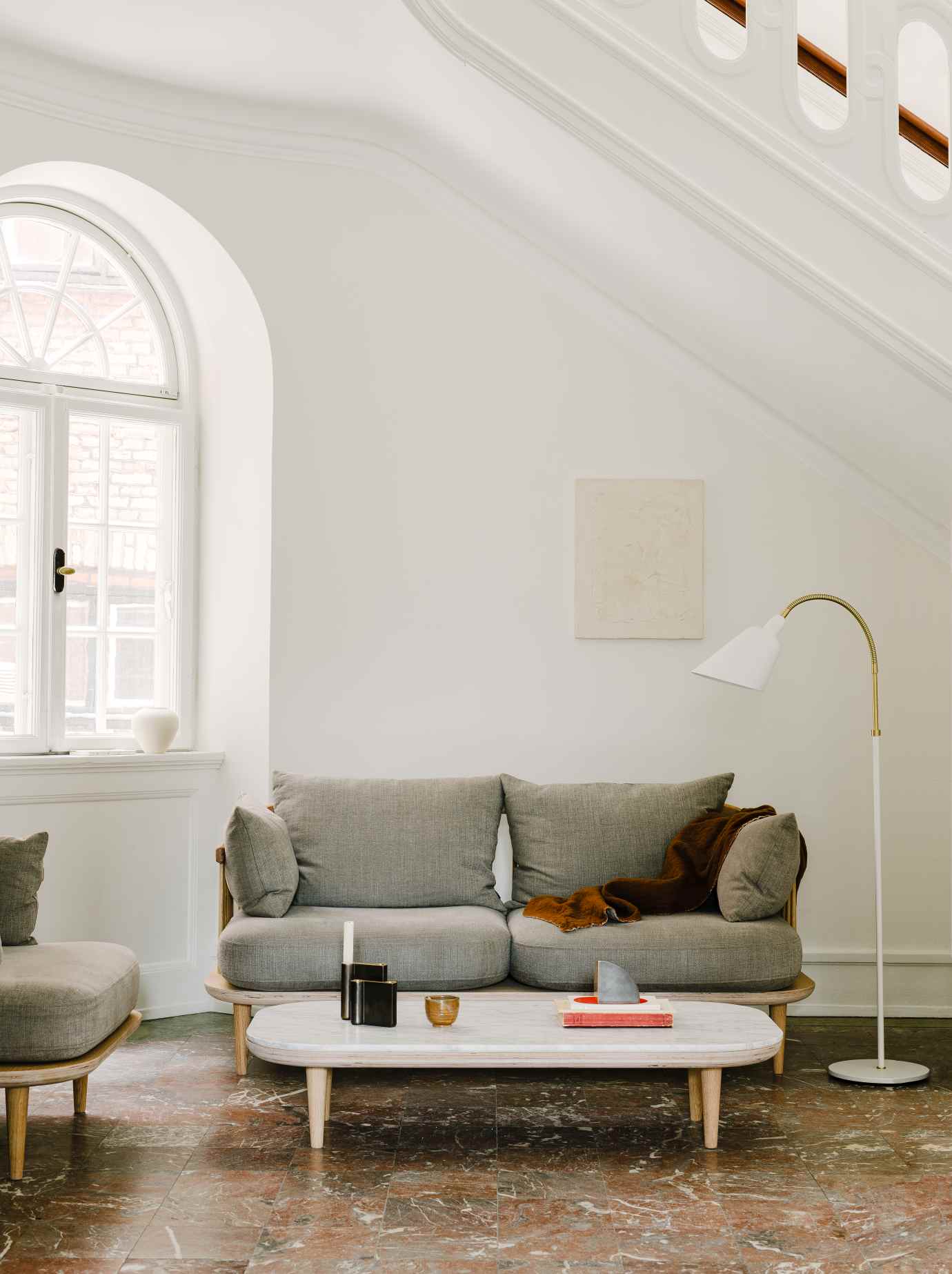 Wohnzimmer mit grauem Sofa, Marmor Couchtisch (Fly Table) und Stehlampe vor weißer Wand.